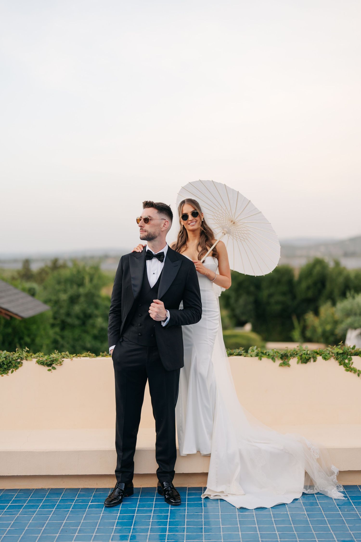 Wedding couple shares playful moments by a pool with a white parasol.