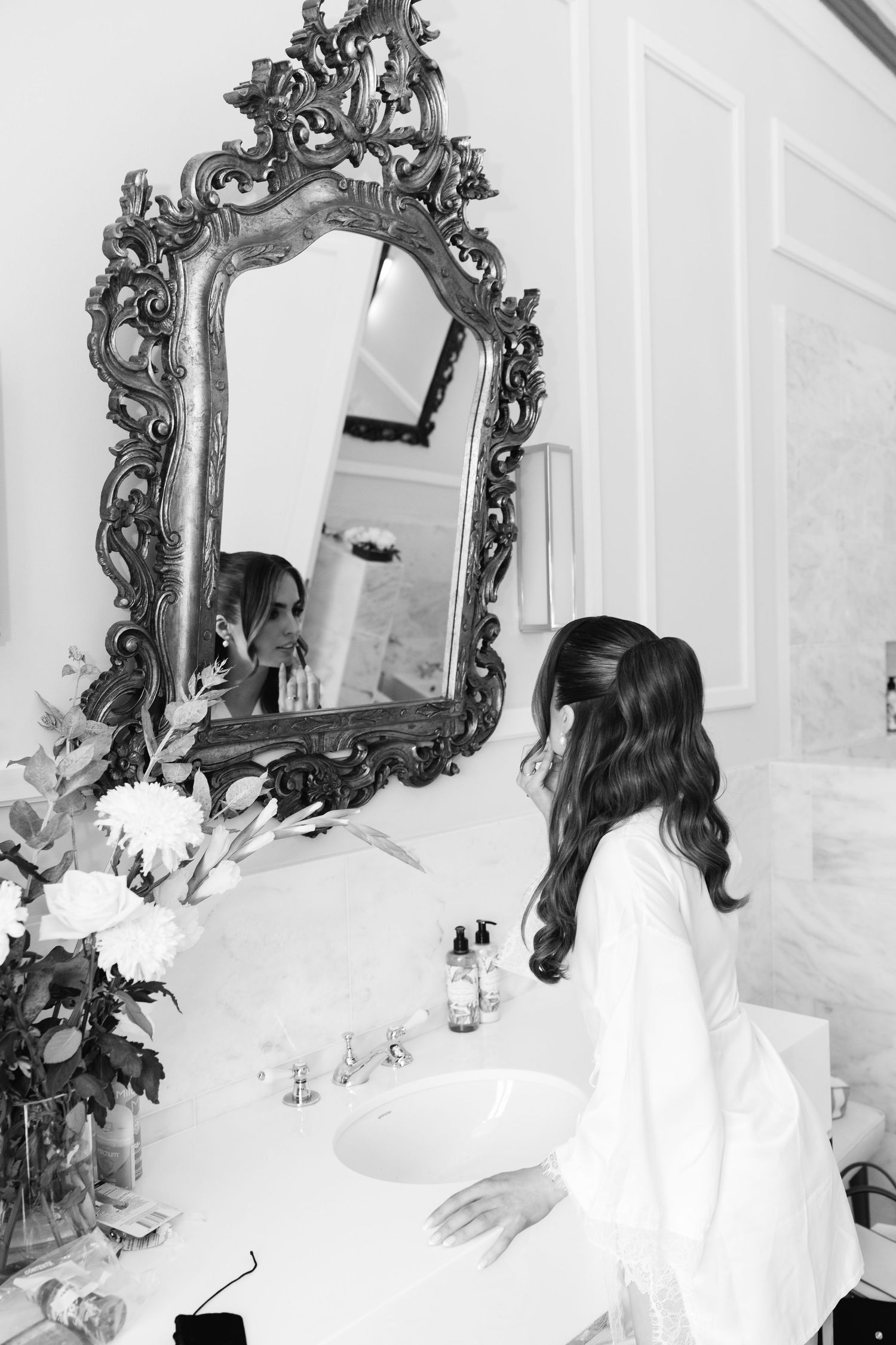 Elegant ornate mirror in black and white with floral arrangement on bathroom vanity.