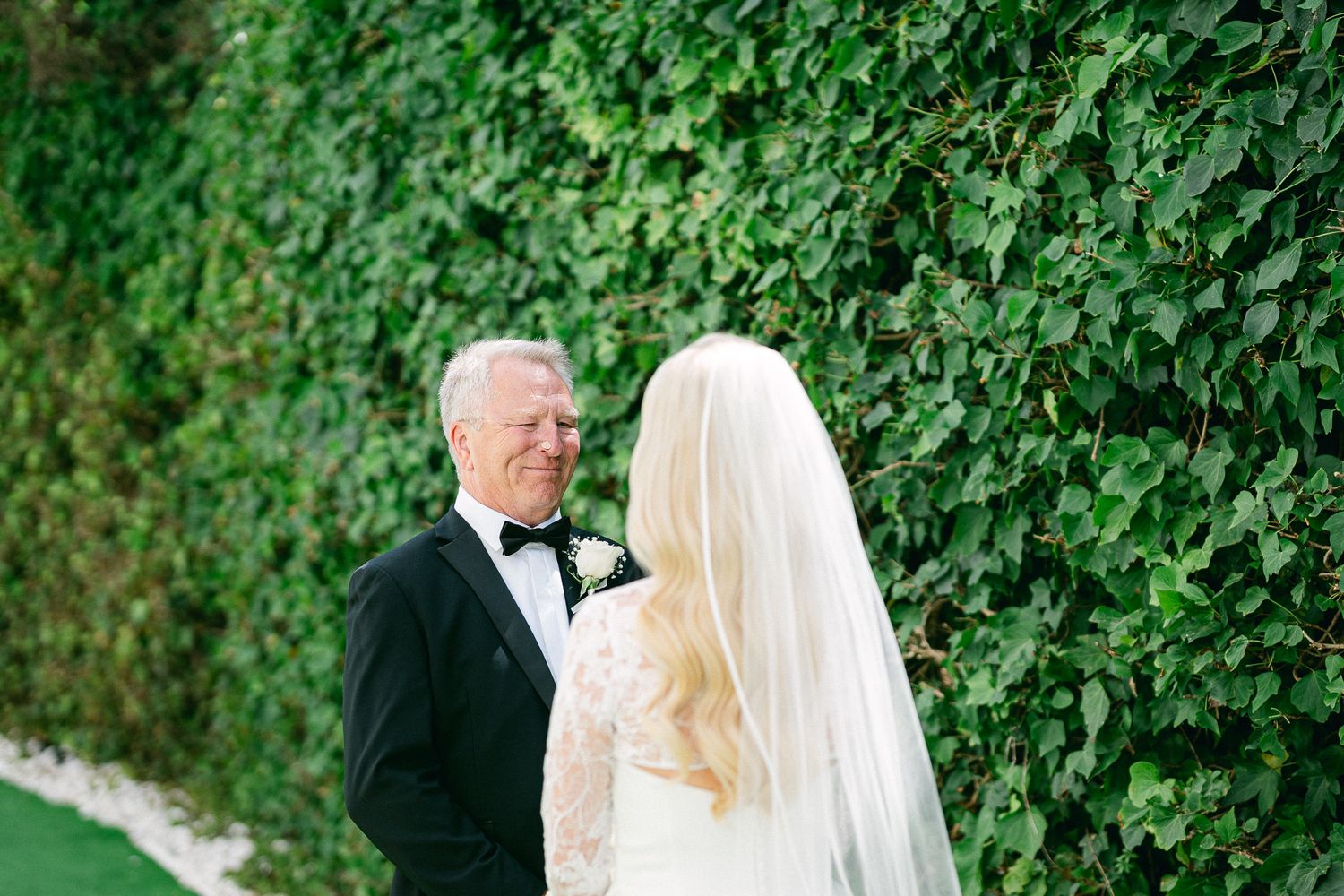 A bride and her escort share a tender moment before the ceremony against an ivy-covered wall.
