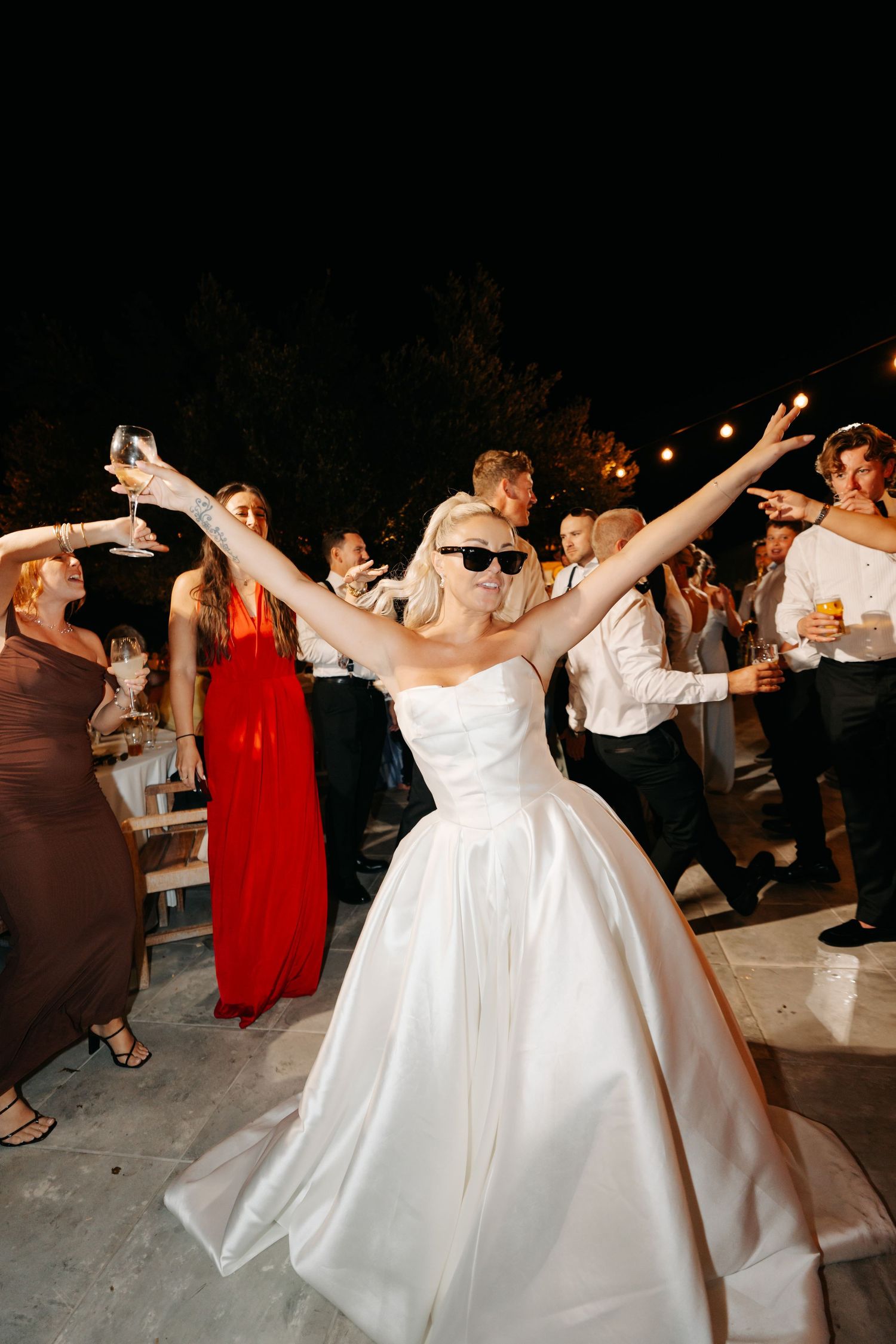 Wedding celebration on a dance floor with people dancing in formal attire and white gowns.
