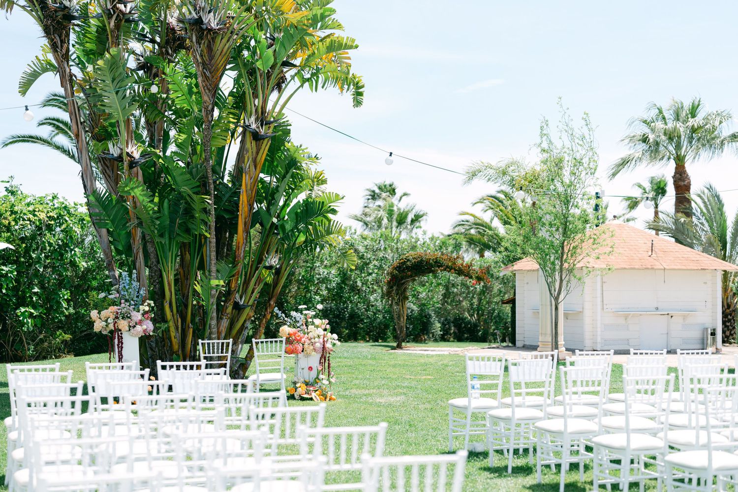 White chairs set up for an outdoor wedding ceremony with tropical palm trees in the background.