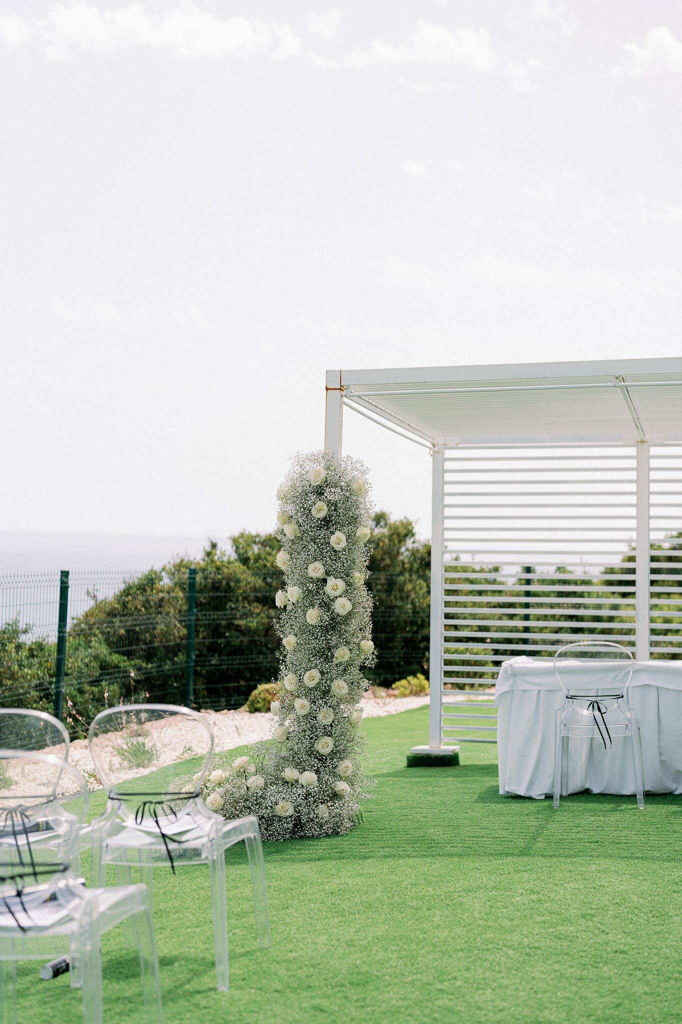 Elegant outdoor wedding reception setup with white pergolas and clear chairs on a grassy lawn.