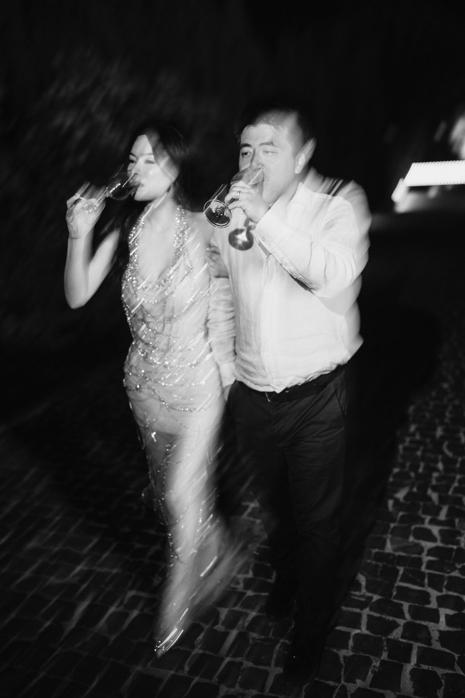 A couple dancing and drinking at a nighttime celebration on a cobblestone street.