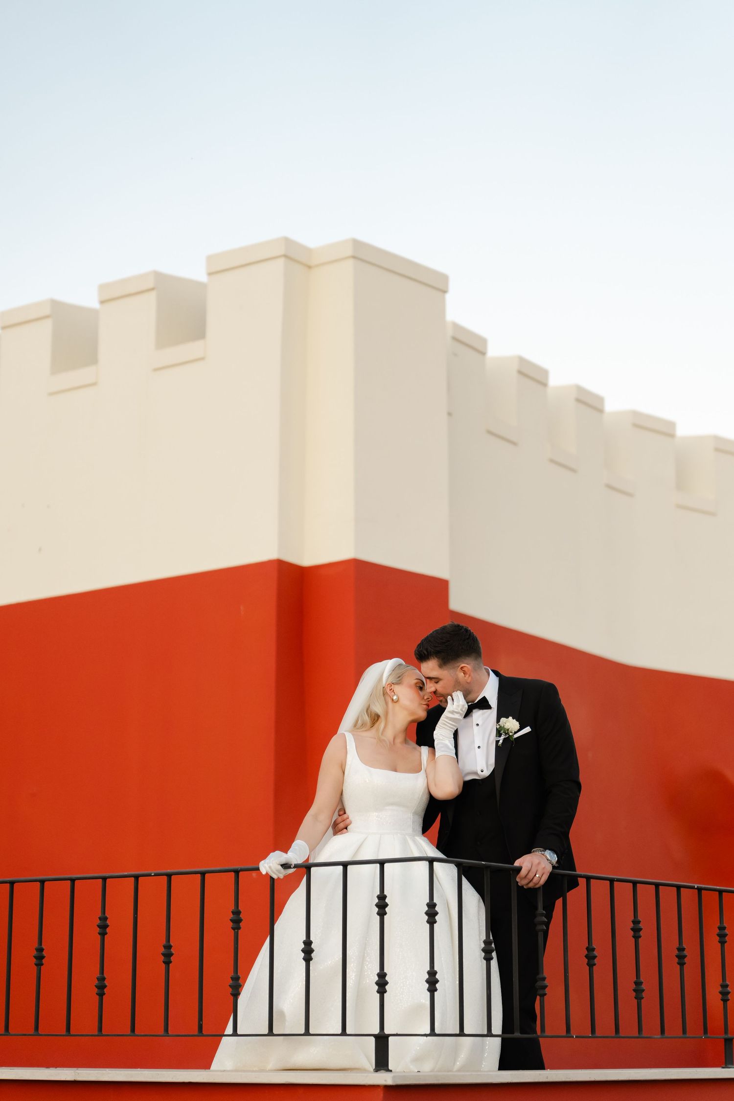 Romantic wedding pose on a geometric red and white castle-like balcony.