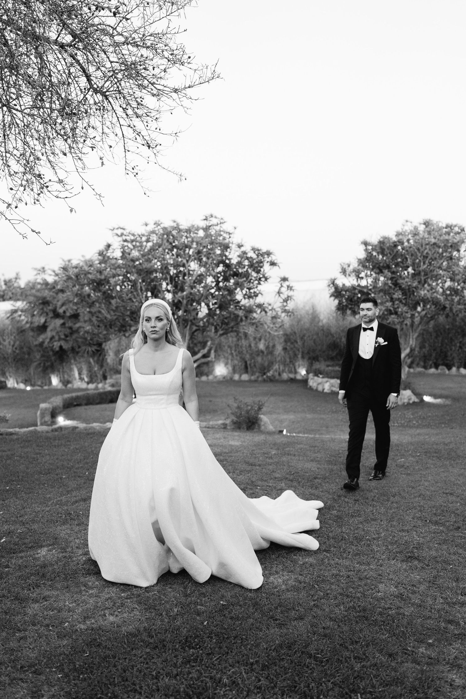 A black and white capture of a bride and groom walking through a garden landscape.
