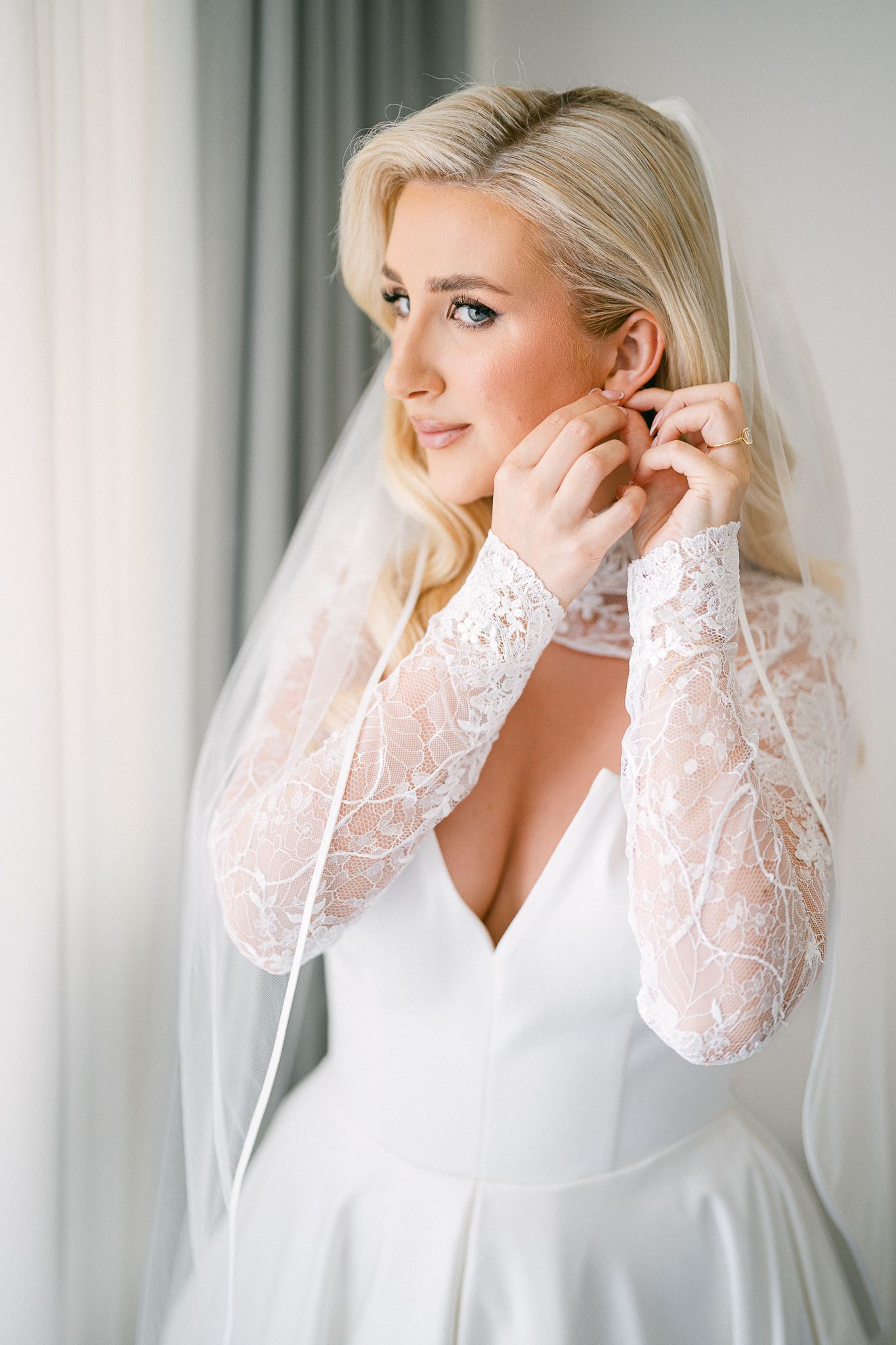 Elegant bridal portrait showing detailed lace sleeves and modern plunging neckline design.