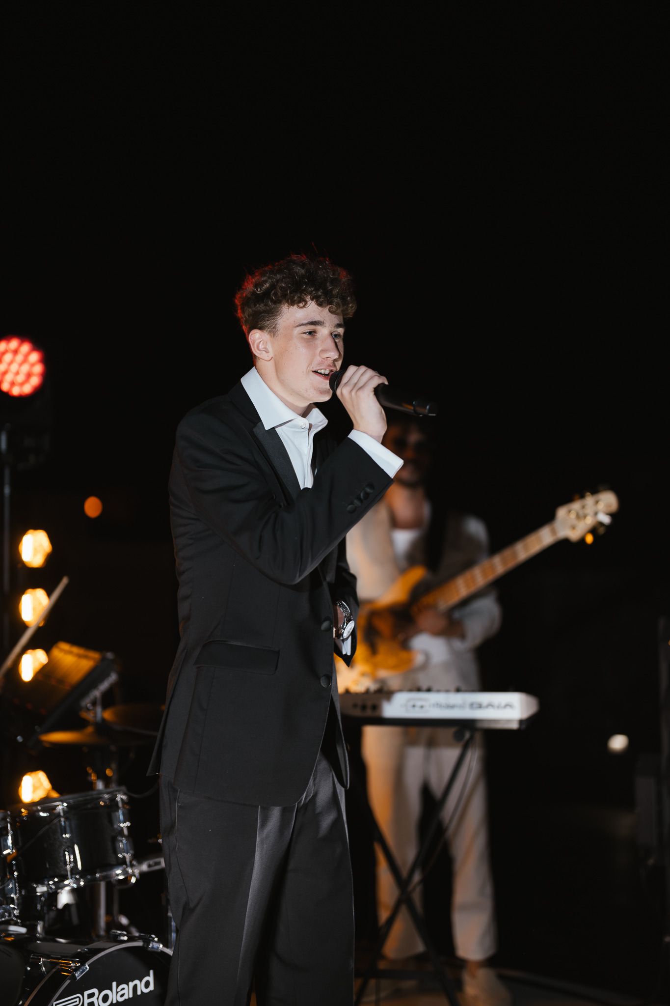 Live band performing at an evening event with instruments and microphone.