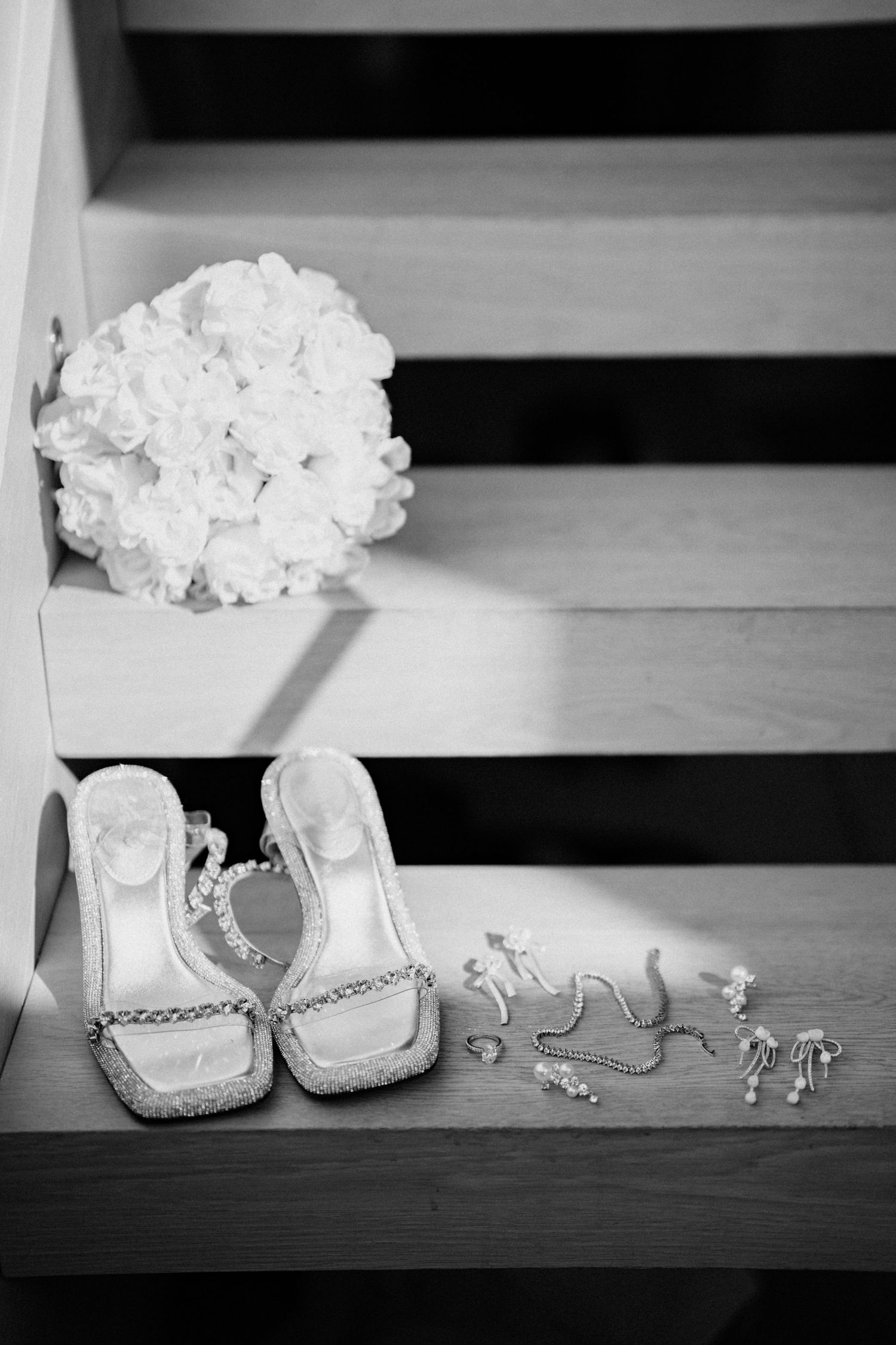 Bridal accessories including white bouquet, crystal shoes and jewelry arranged on wooden steps.