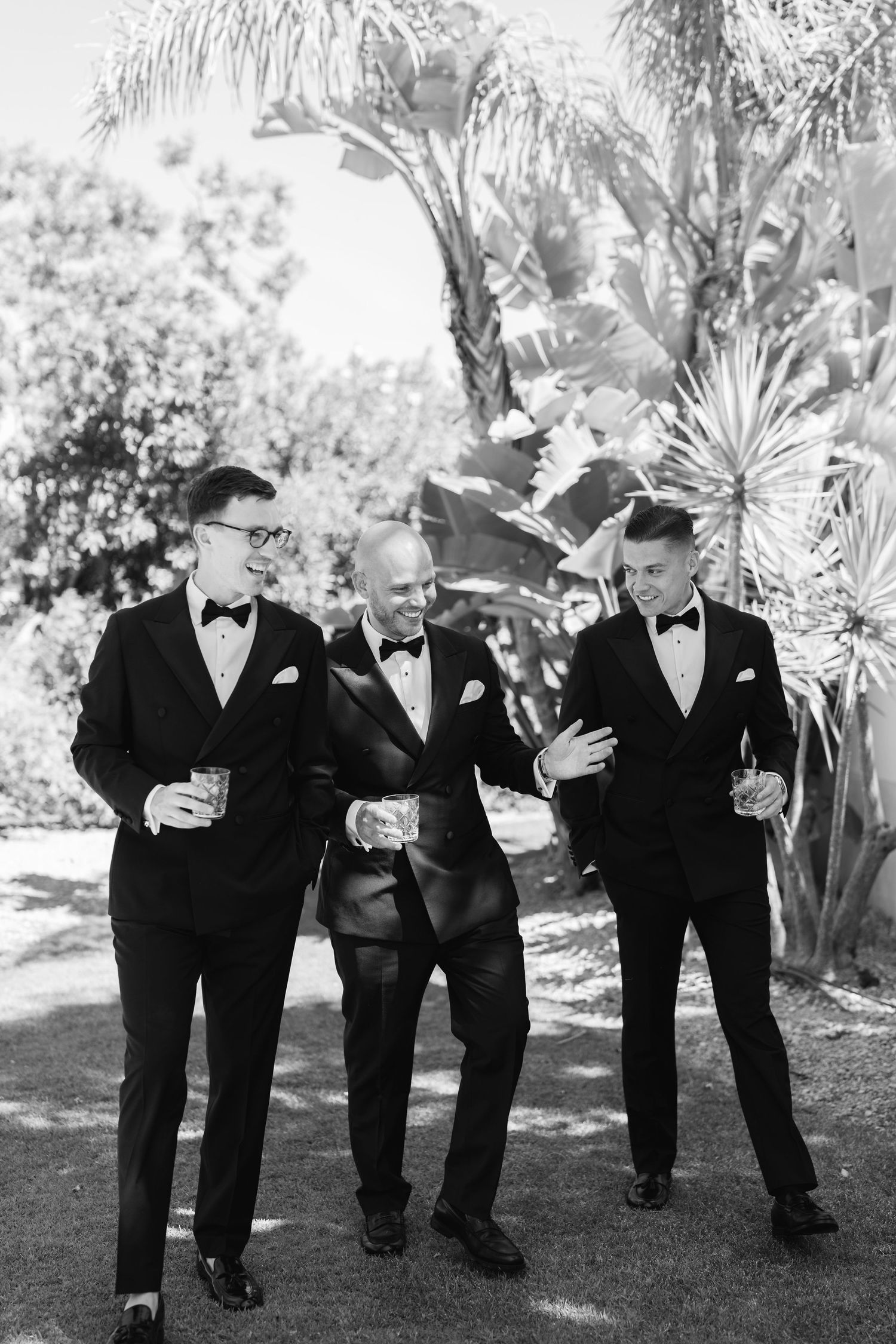 Wedding party in formal attire walking together on garden grounds.