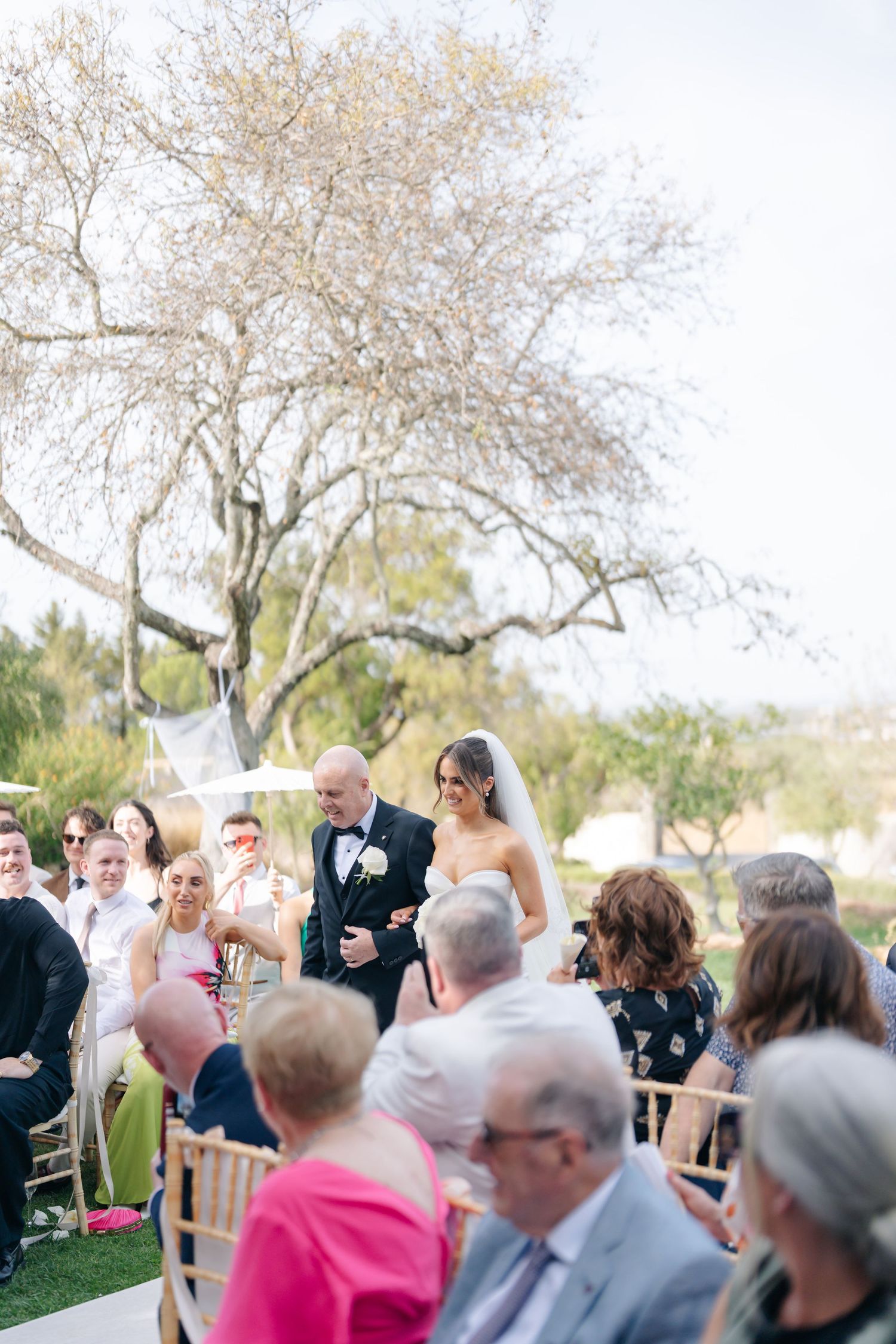 Wedding guests gather under blooming trees during an outdoor ceremony.