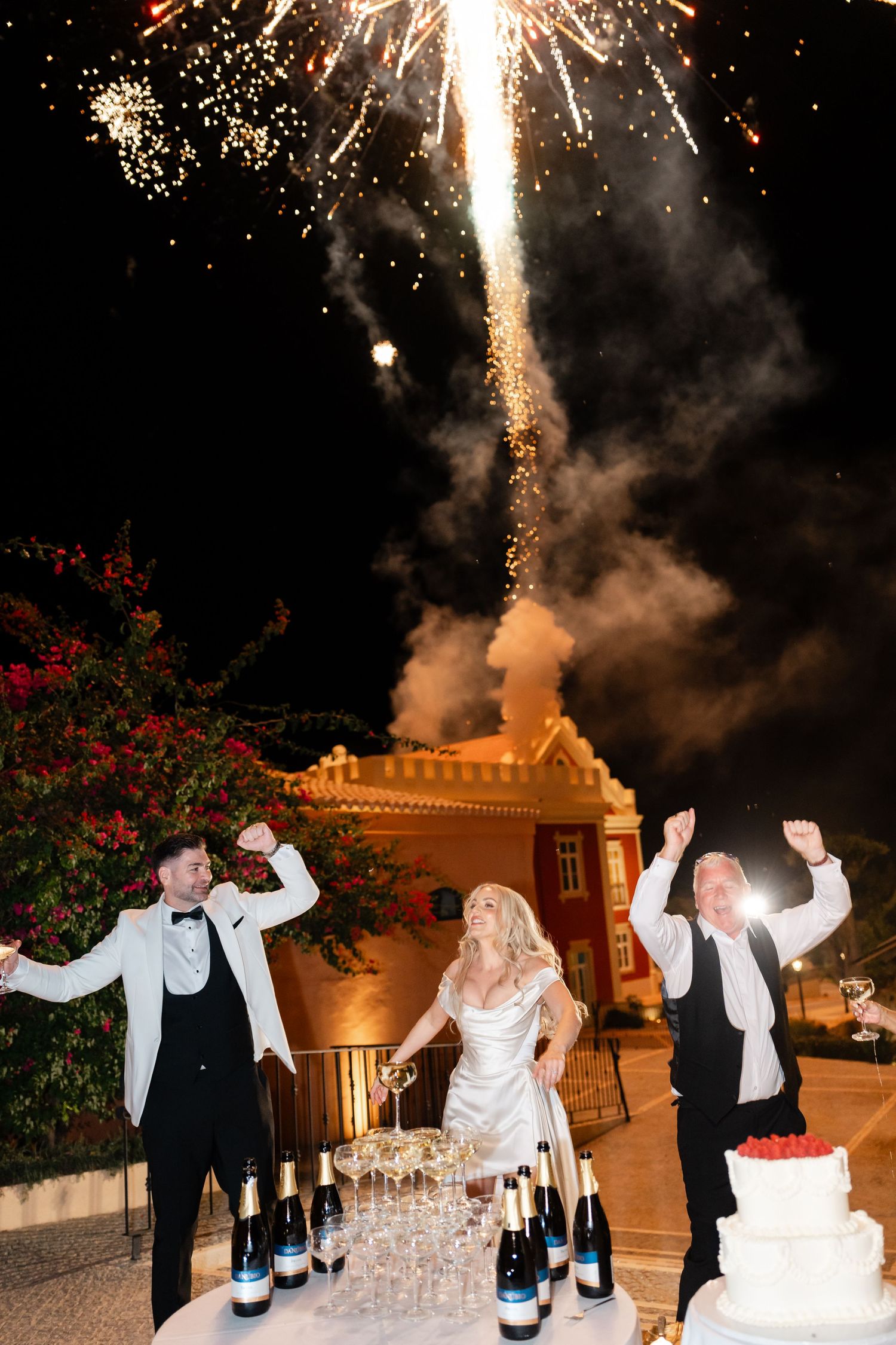 Fireworks illuminate the night sky as newlyweds celebrate with champagne tower.