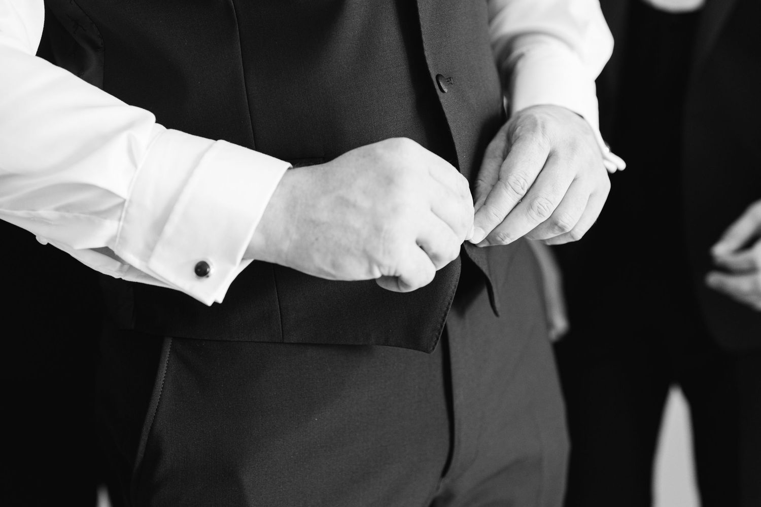 Close up of hands adjusting formal black vest buttons.