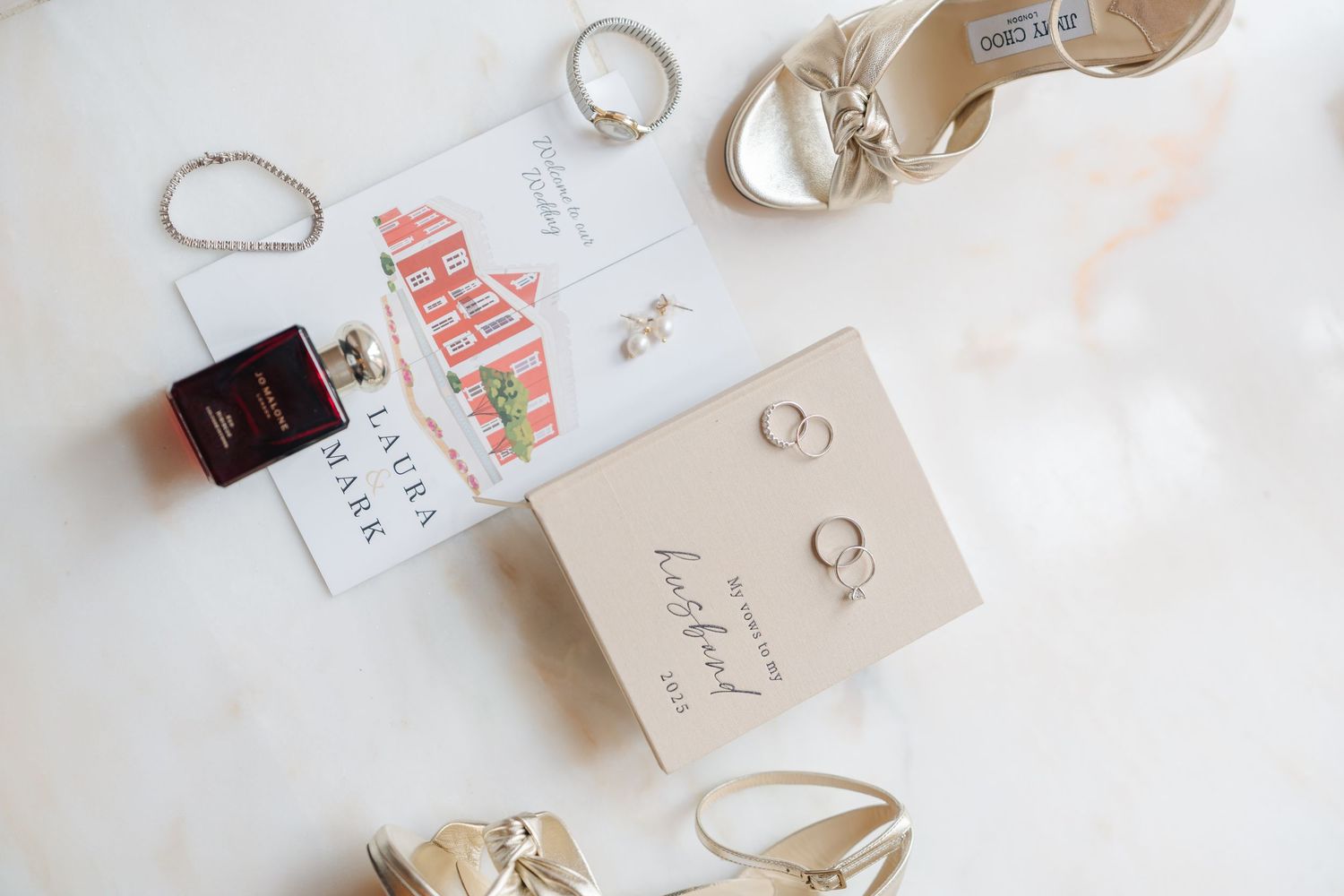 Wedding accessories including rings, shoes, and invitation cards arranged on white surface.