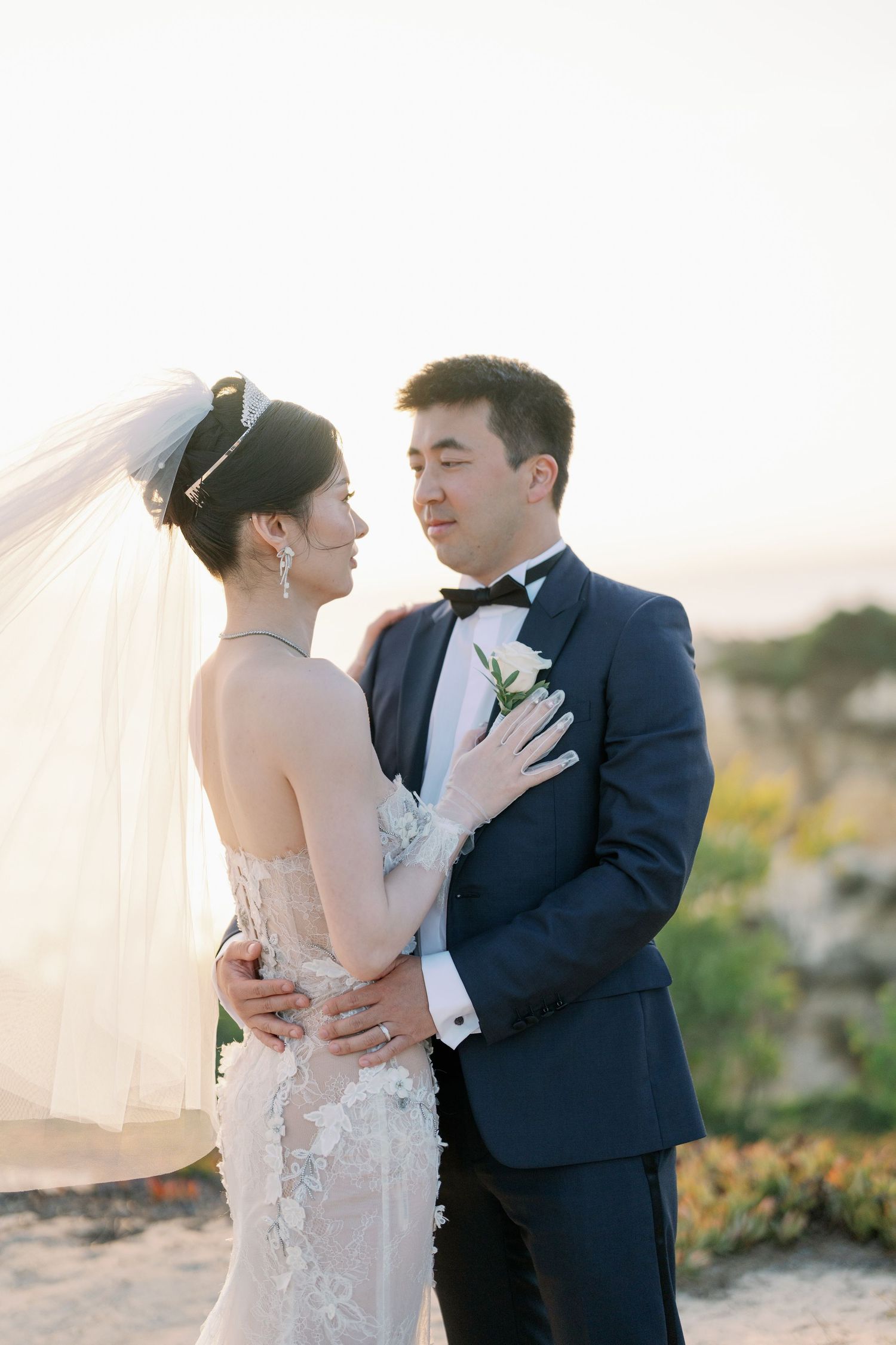 Romantic sunset portrait of newlyweds embracing in formal wedding attire.