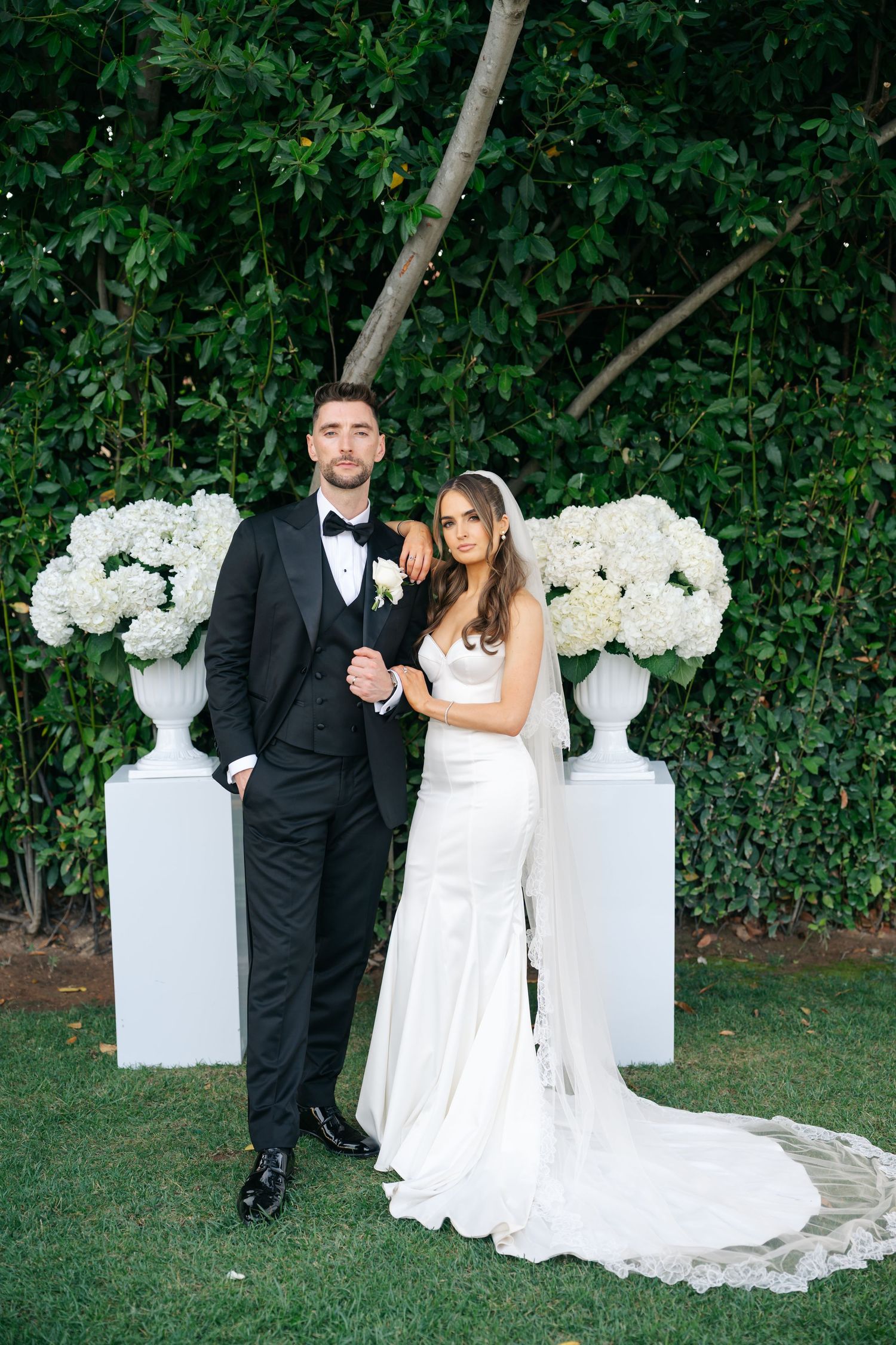 Elegant wedding portraits with white floral urns and lush garden backdrop.