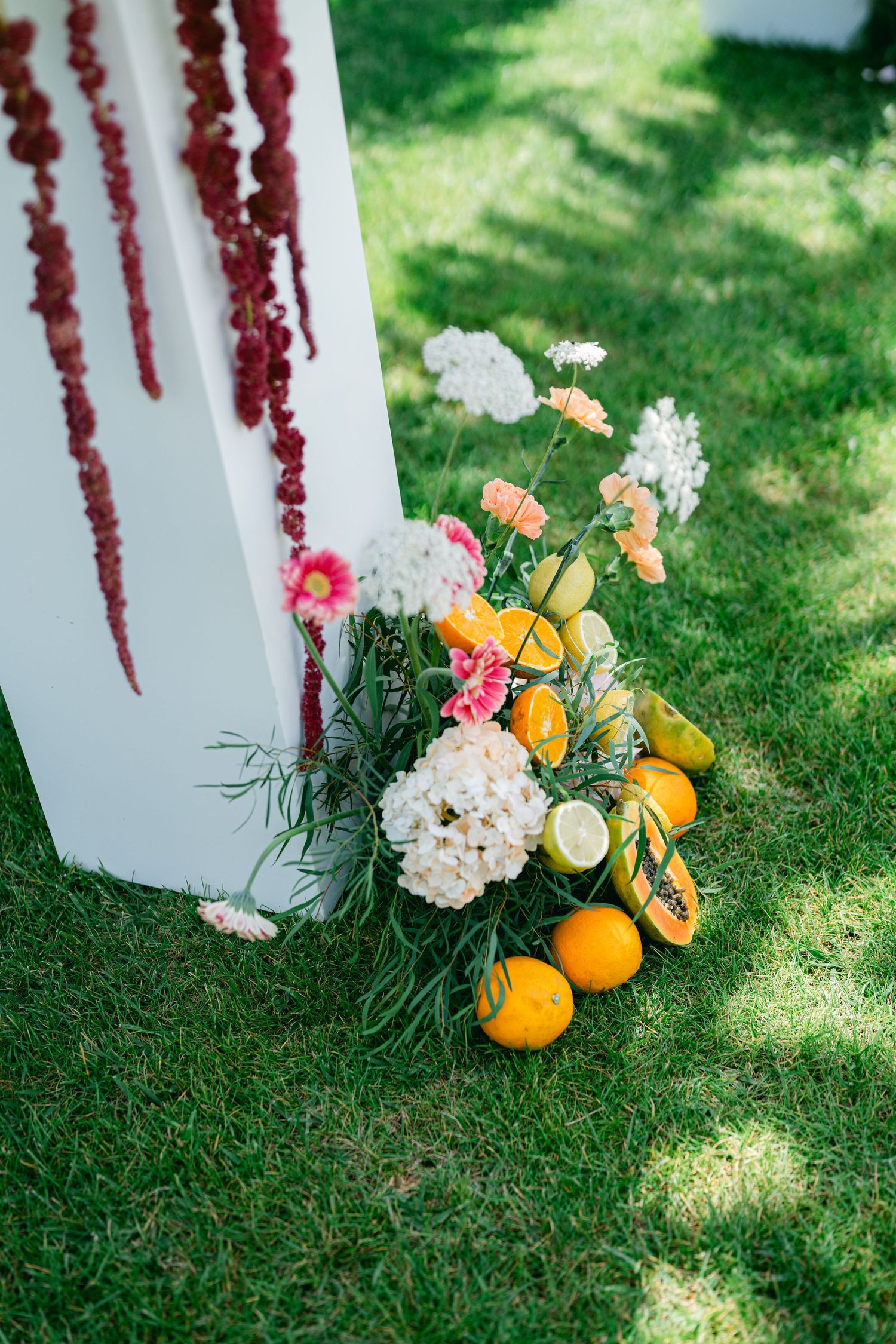 Fresh citrus fruits and white floral arrangements rest on lush green grass beside white columns.
