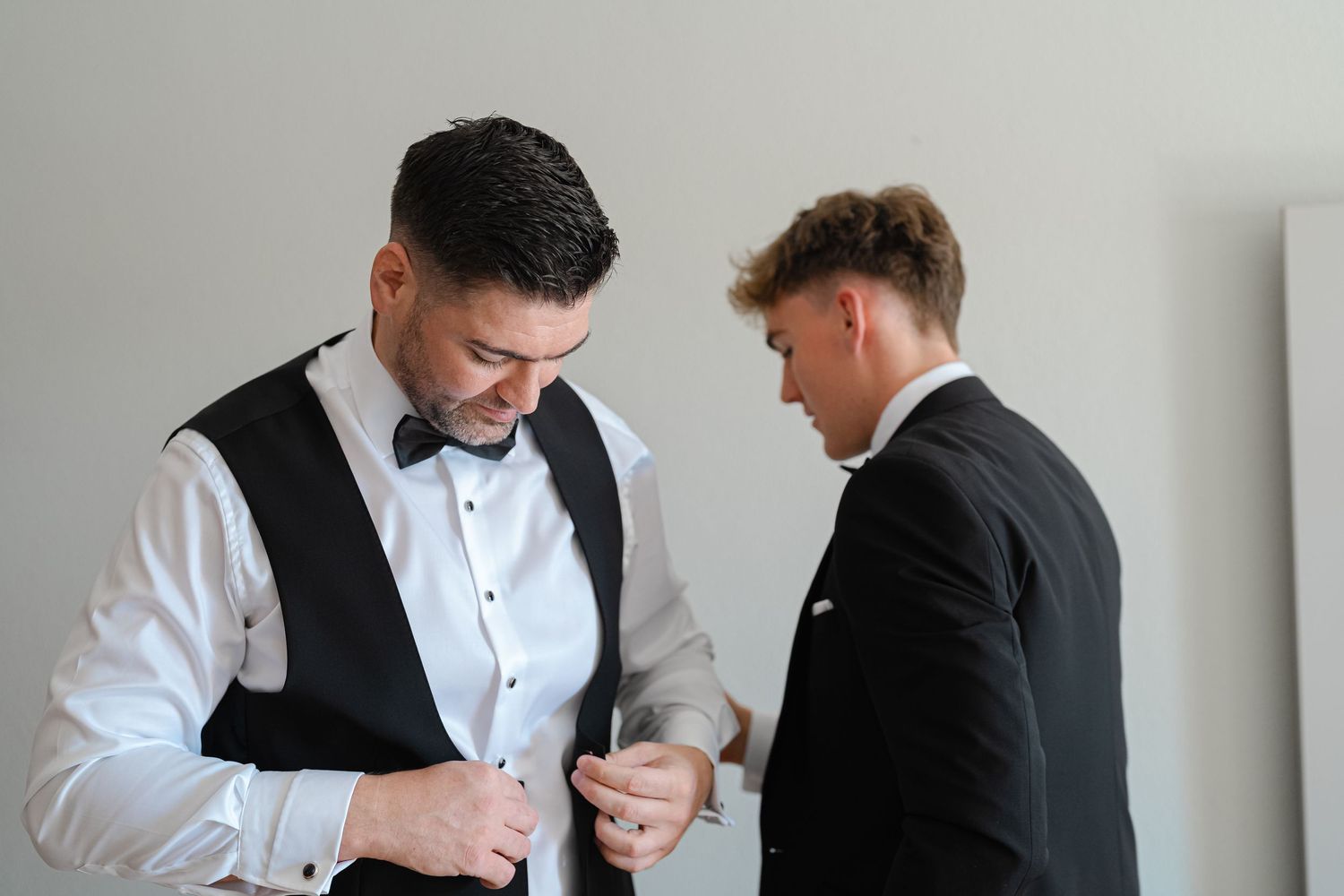 Two people in formal attire adjusting clothing before event.