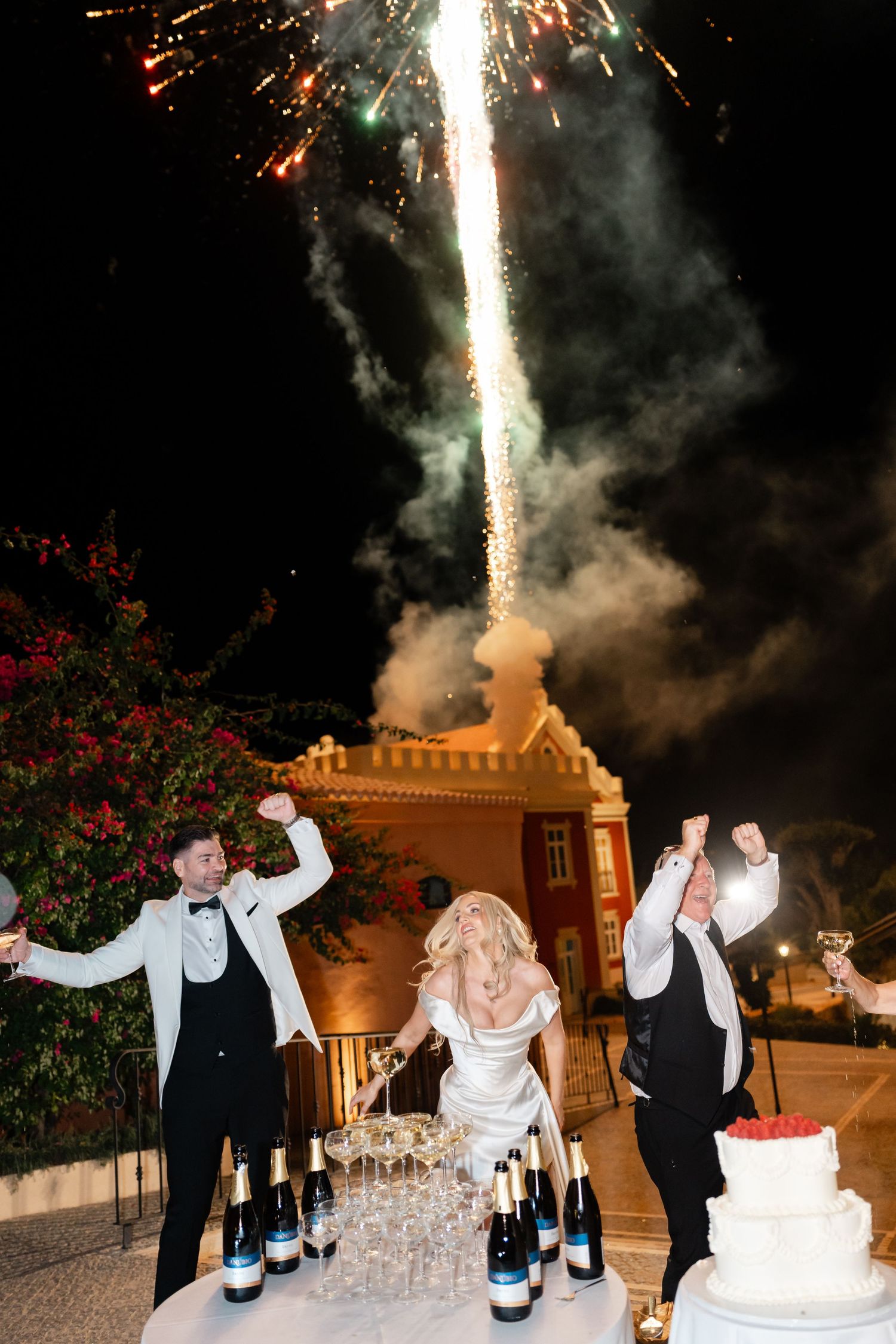 Wedding celebration with champagne tower and fireworks display in background.