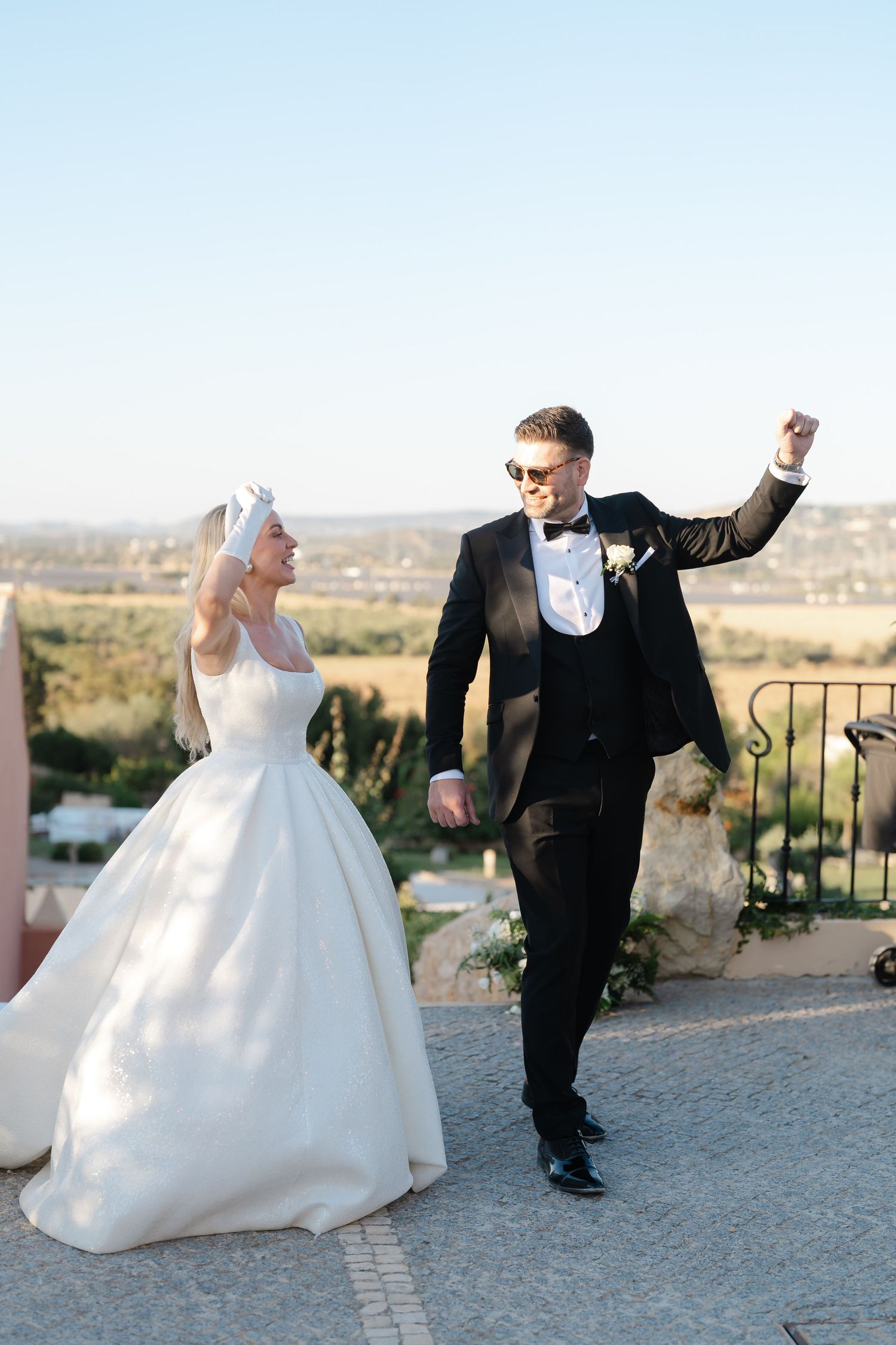 Playful wedding couple dancing and twirling on a stone patio with scenic views.