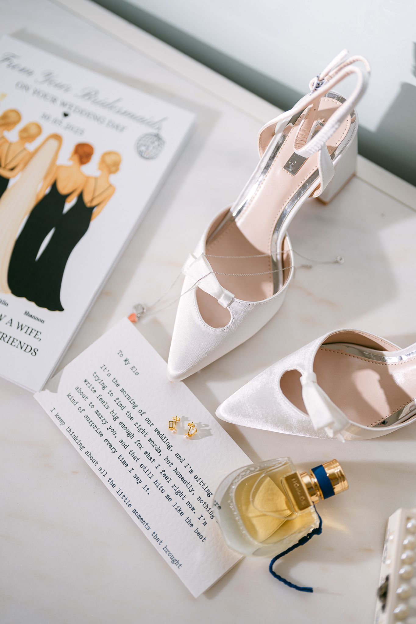 Wedding accessories including white heels, handwritten notes, and perfume bottle arranged on white surface.