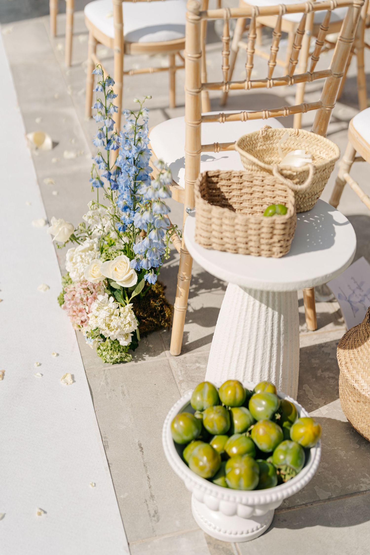 Wedding decor featuring wooden chairs, blue flowers, and fresh citrus fruits in white bowls.