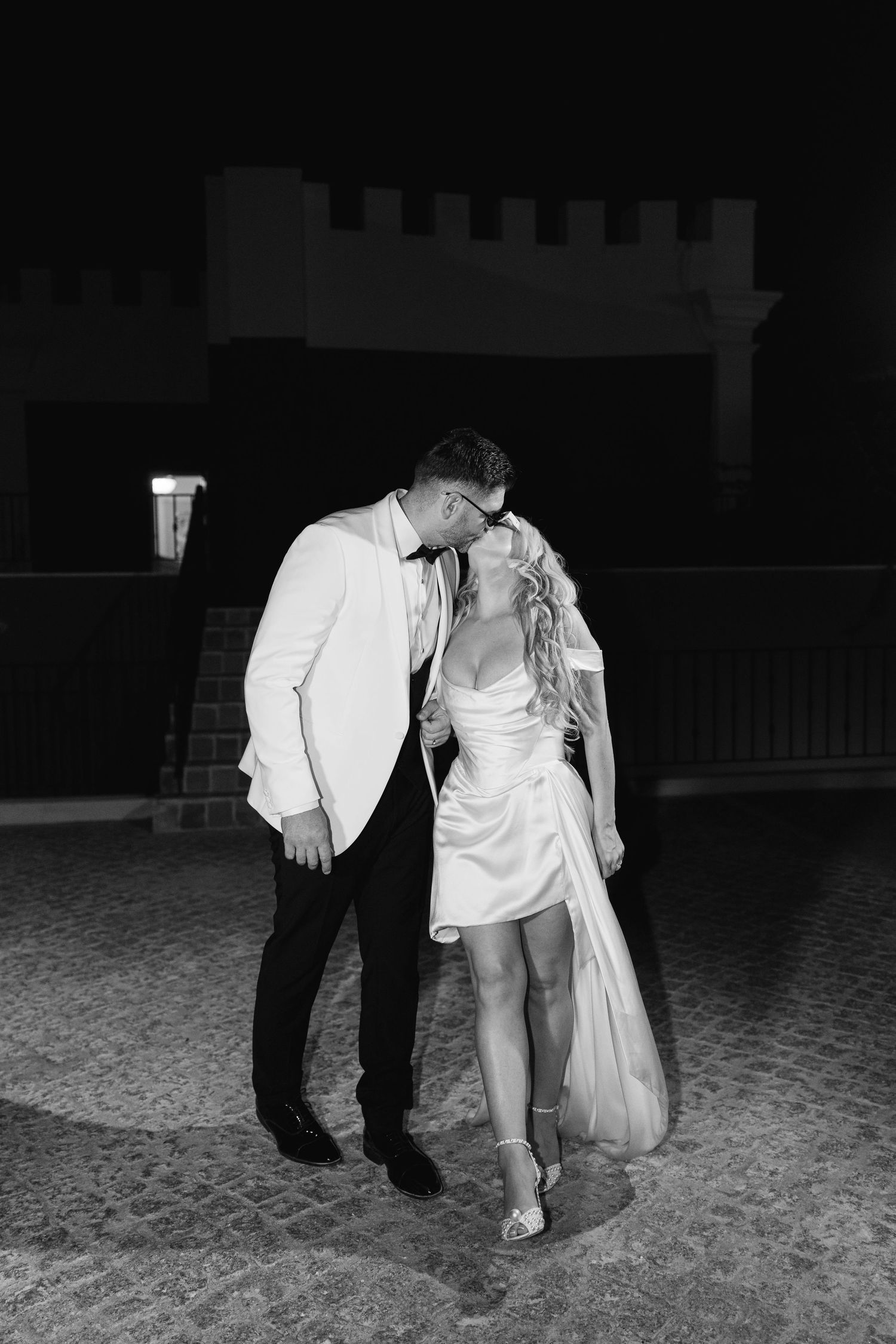 A couple in black and white formal attire dancing together on a dark outdoor surface.