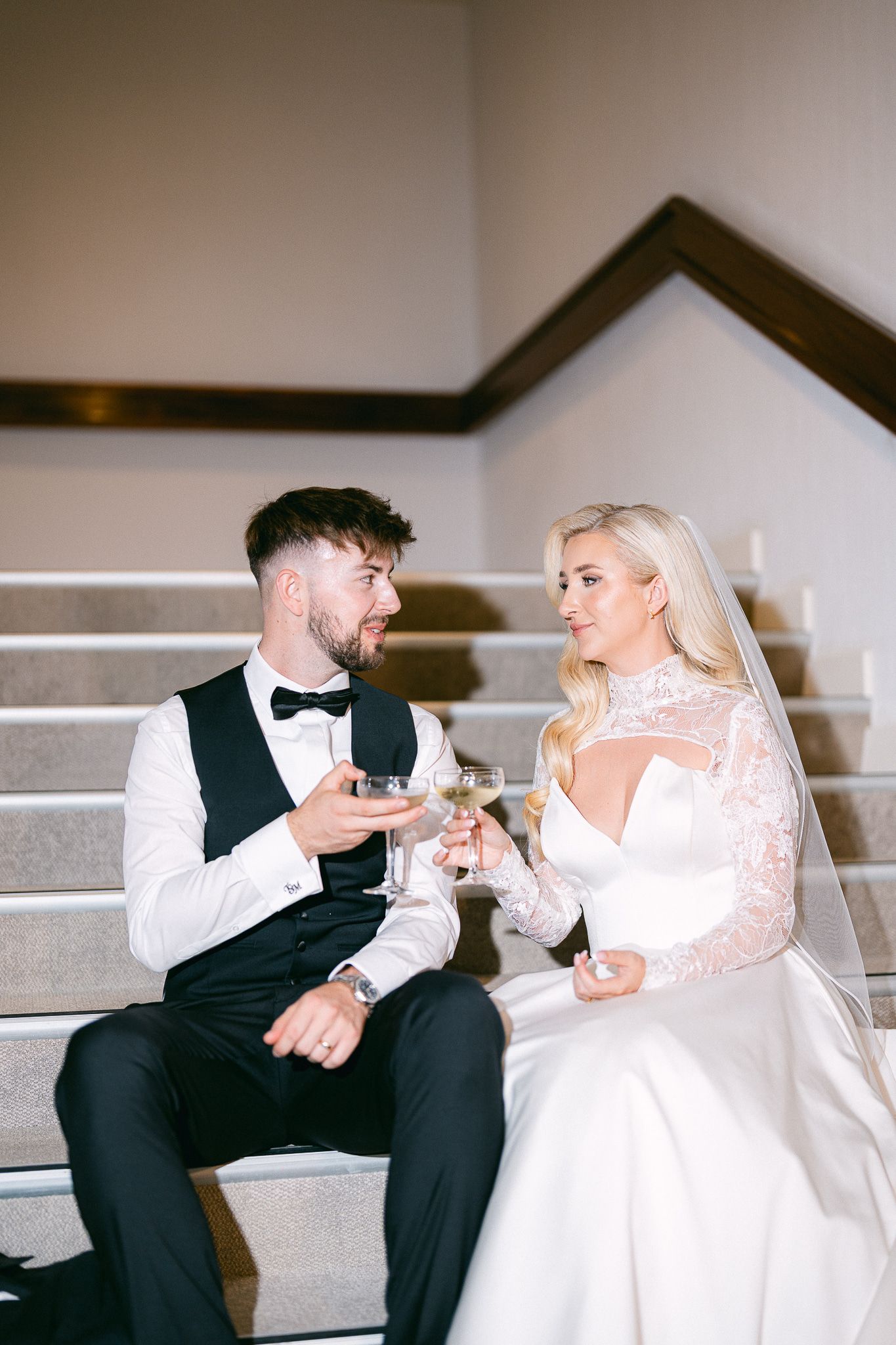Newlyweds sit on stairs sharing drinks and conversation at their reception.