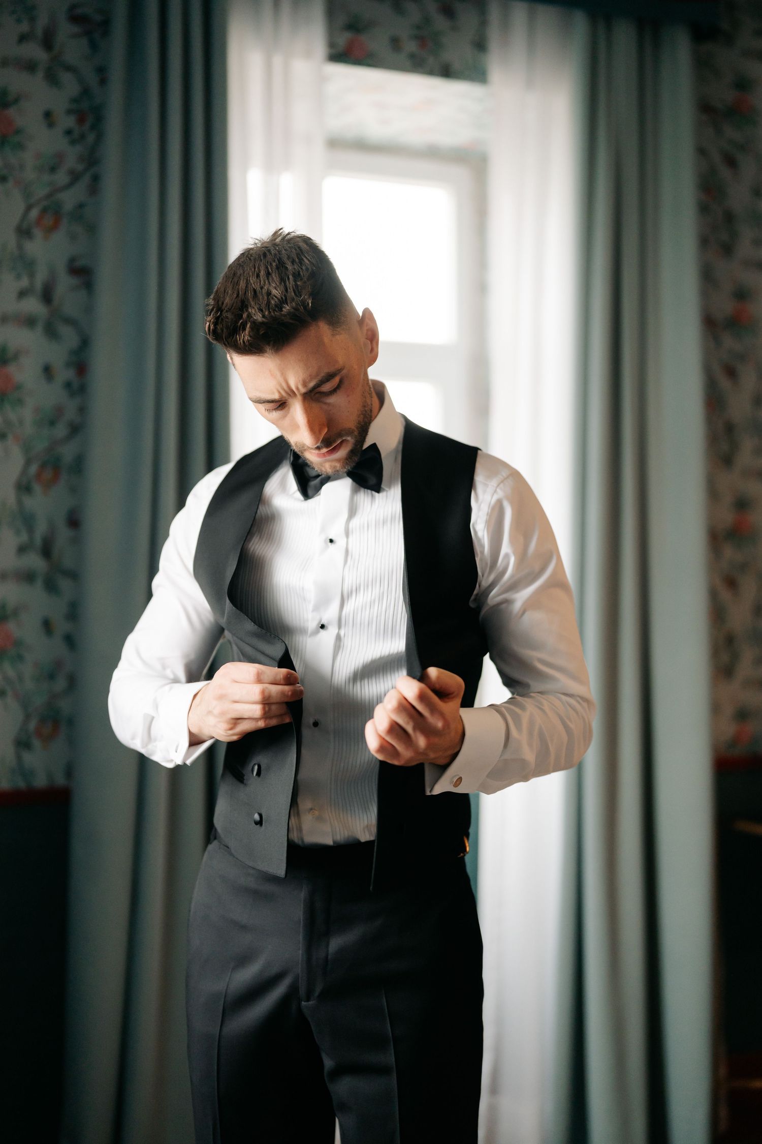 Groom adjusts his vest while getting ready in formal attire.