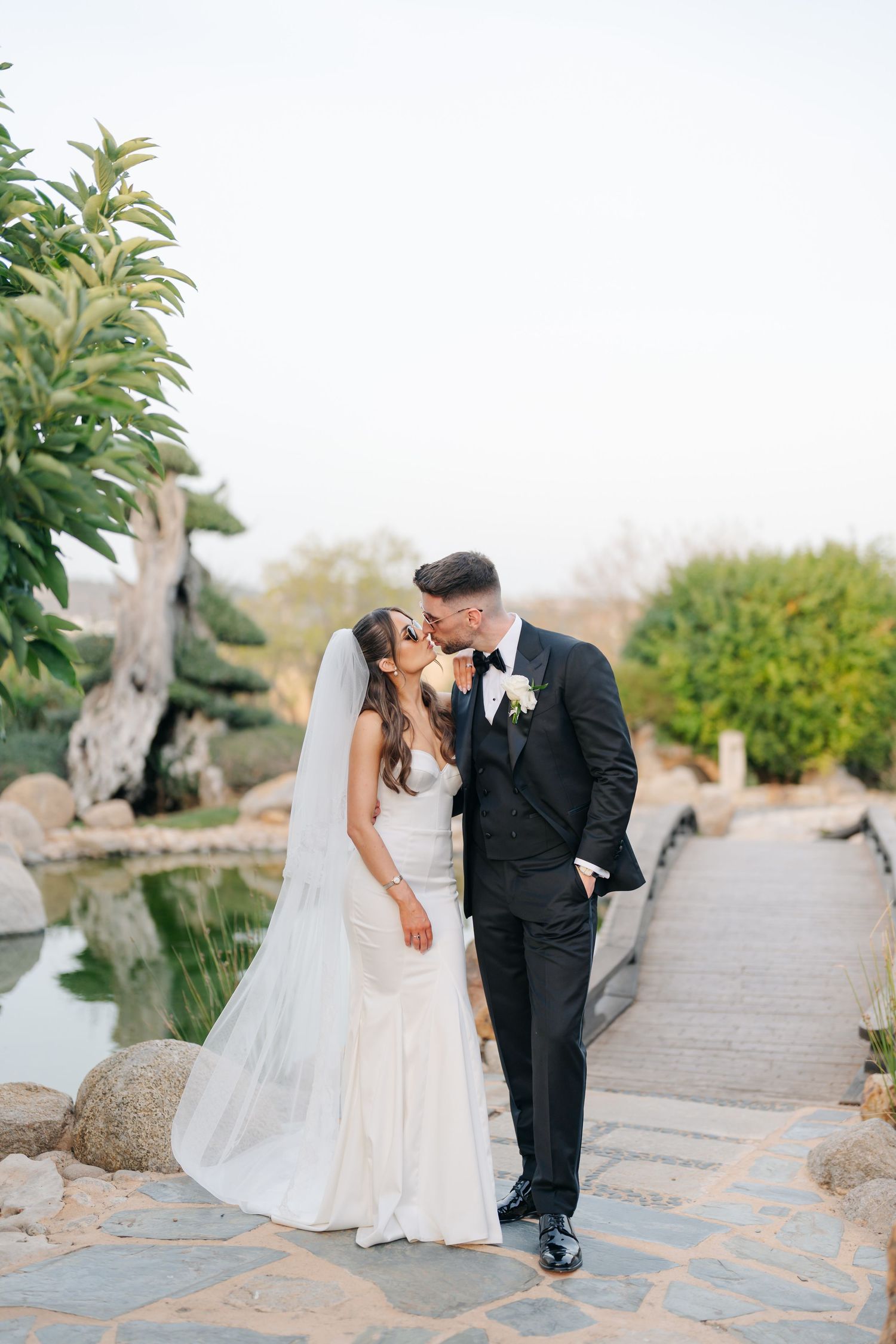 A romantic wedding couple shares a moment on a stone path surrounded by greenery.