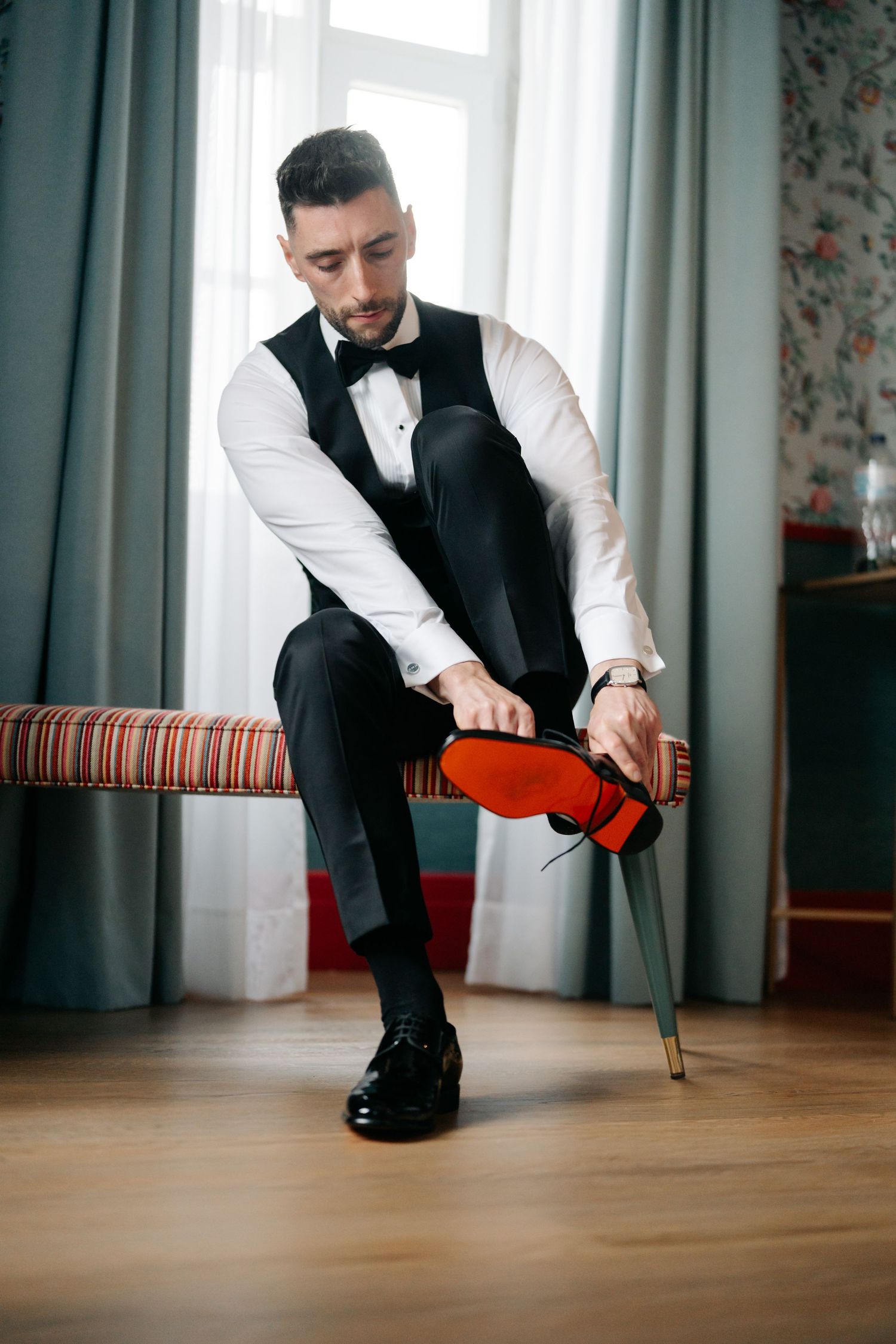 Formal attire with attention to red-soled dress shoes while seated on striped bench.