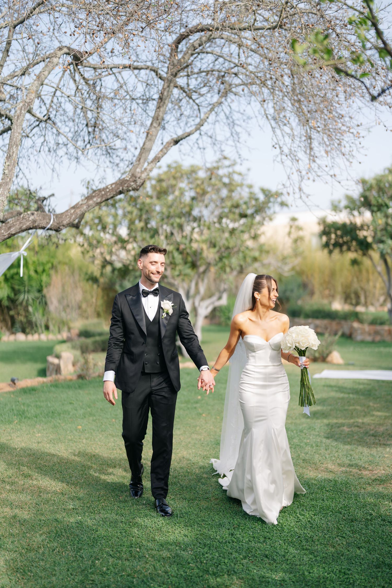 Couple walking together on grassy path during their wedding photoshoot.