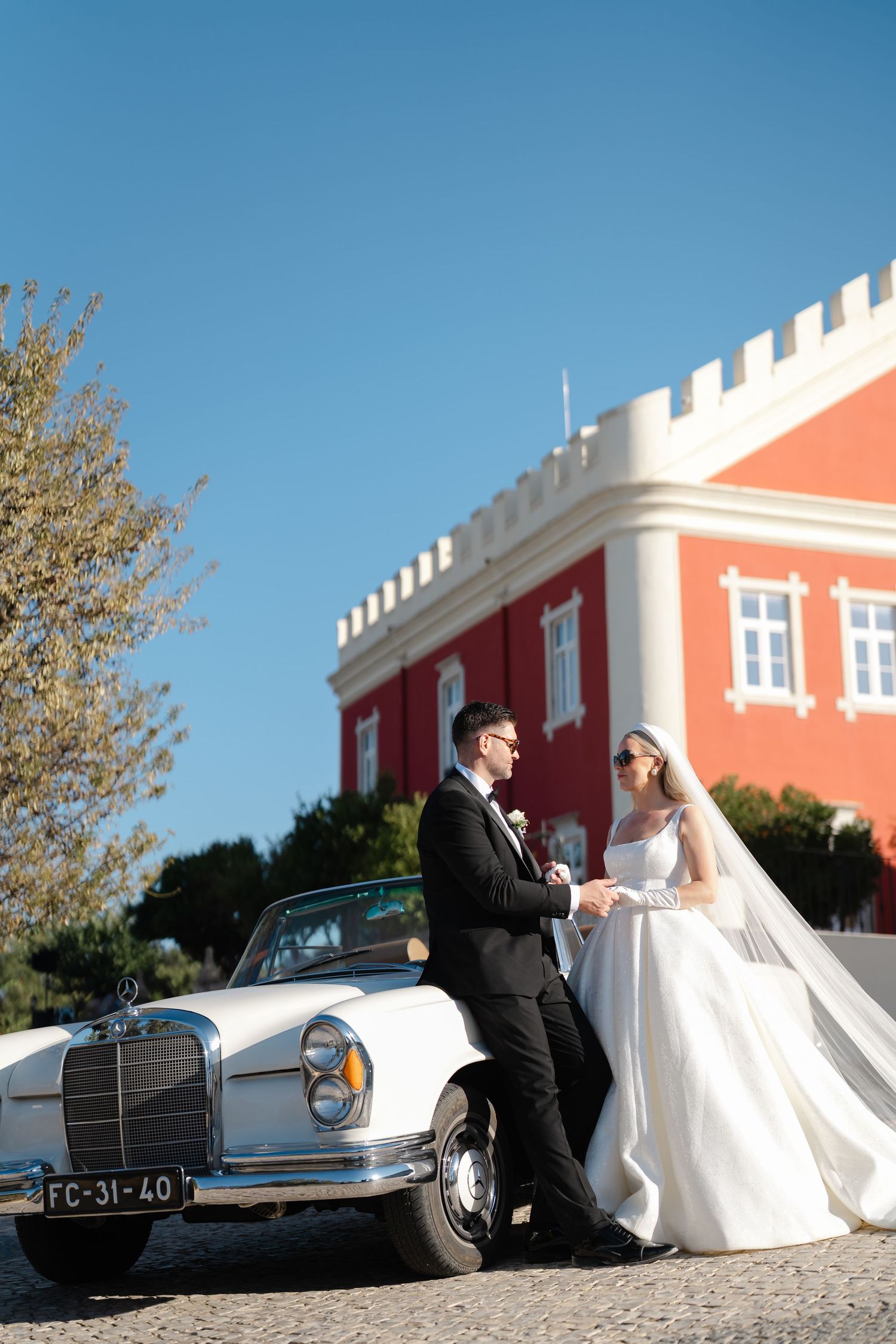 Elegant wedding photo with vintage Mercedes-Benz and coral building backdrop.