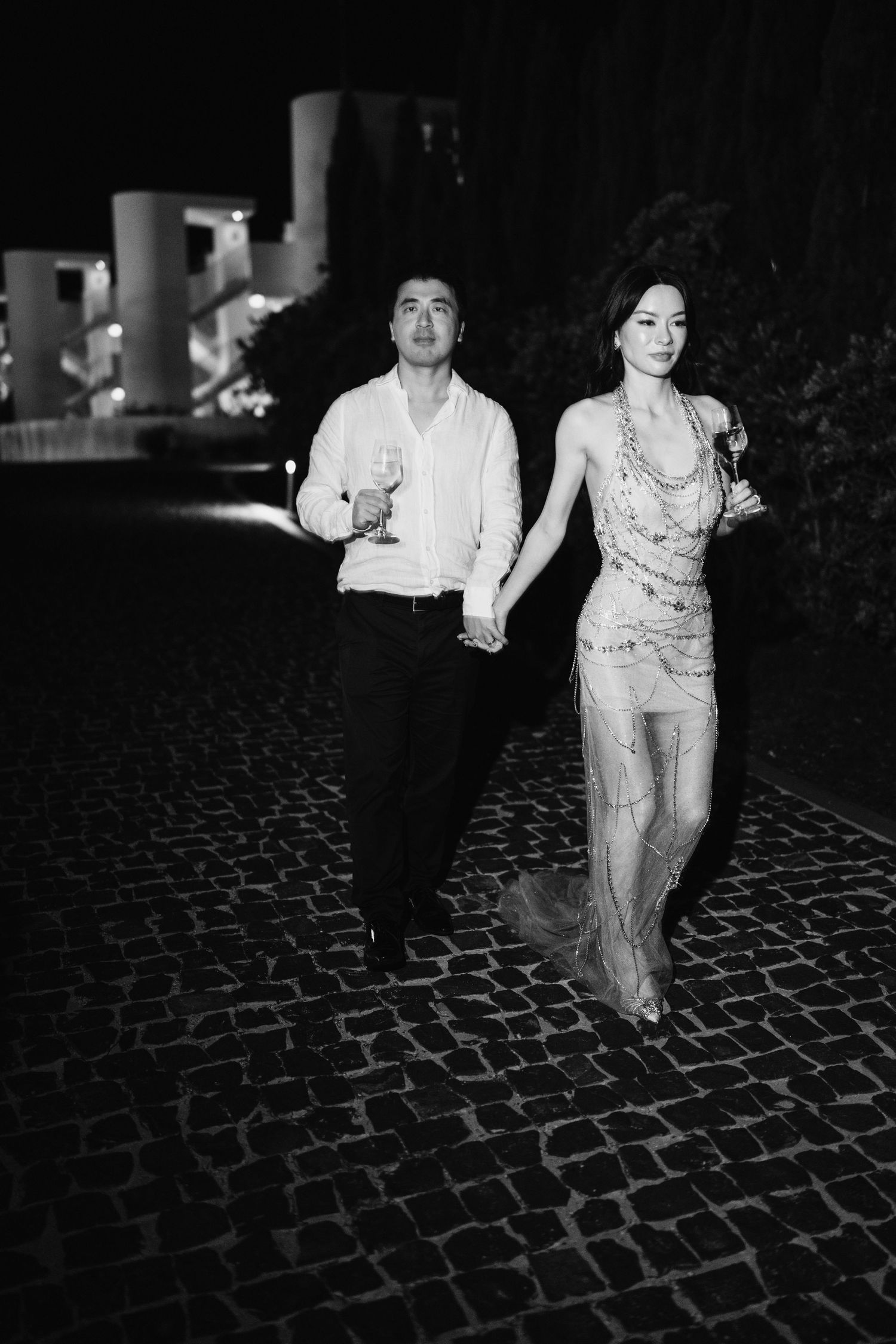 Black and white photo of couple running playfully on cobblestone path at night.
