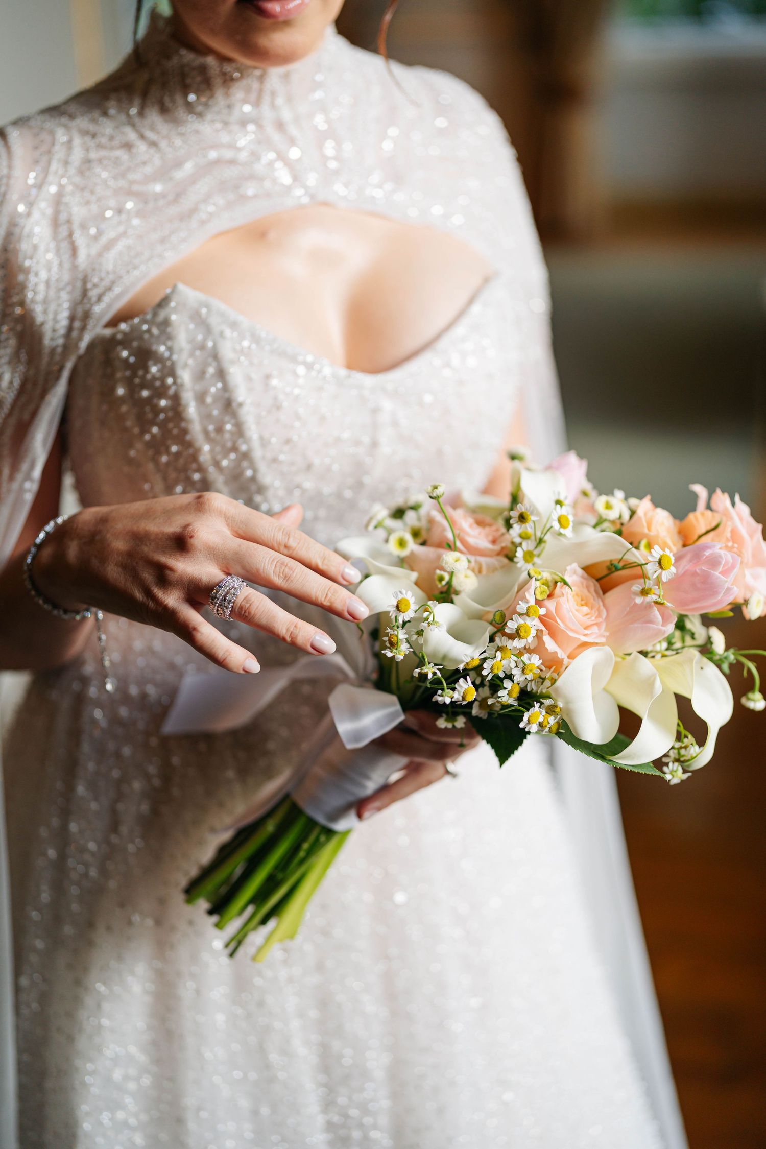 Close-up details of a bridal bouquet featuring delicate peach and pink flowers with sparkly wedding dress fabric.