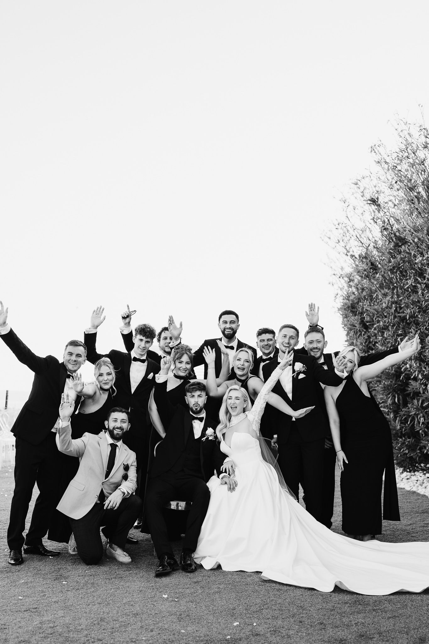 Black and white photo of wedding party making fun poses on outdoor lawn.