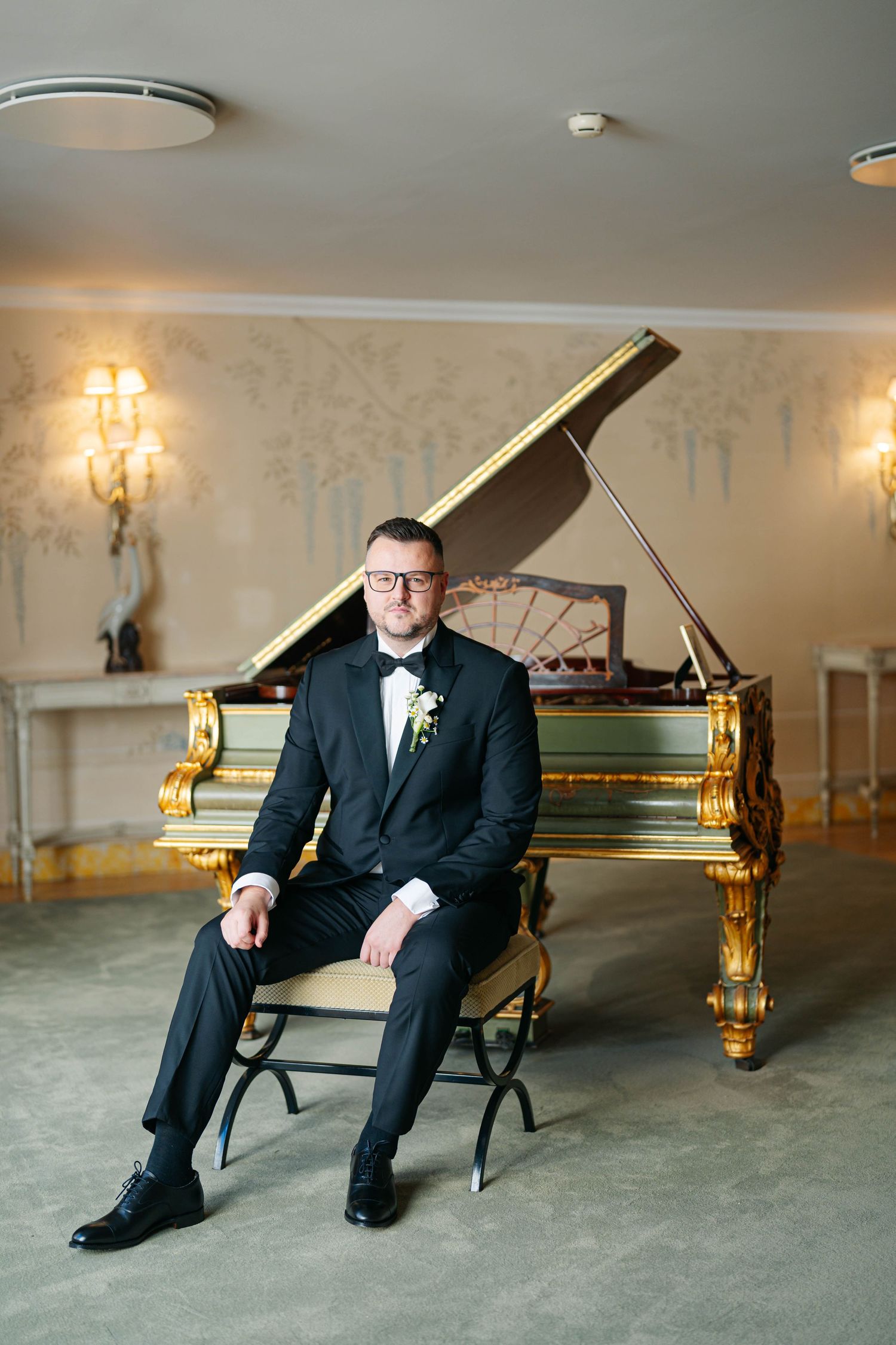Elegant formal portrait with a stunning gold grand piano in an ornate room with crystal wall sconces.