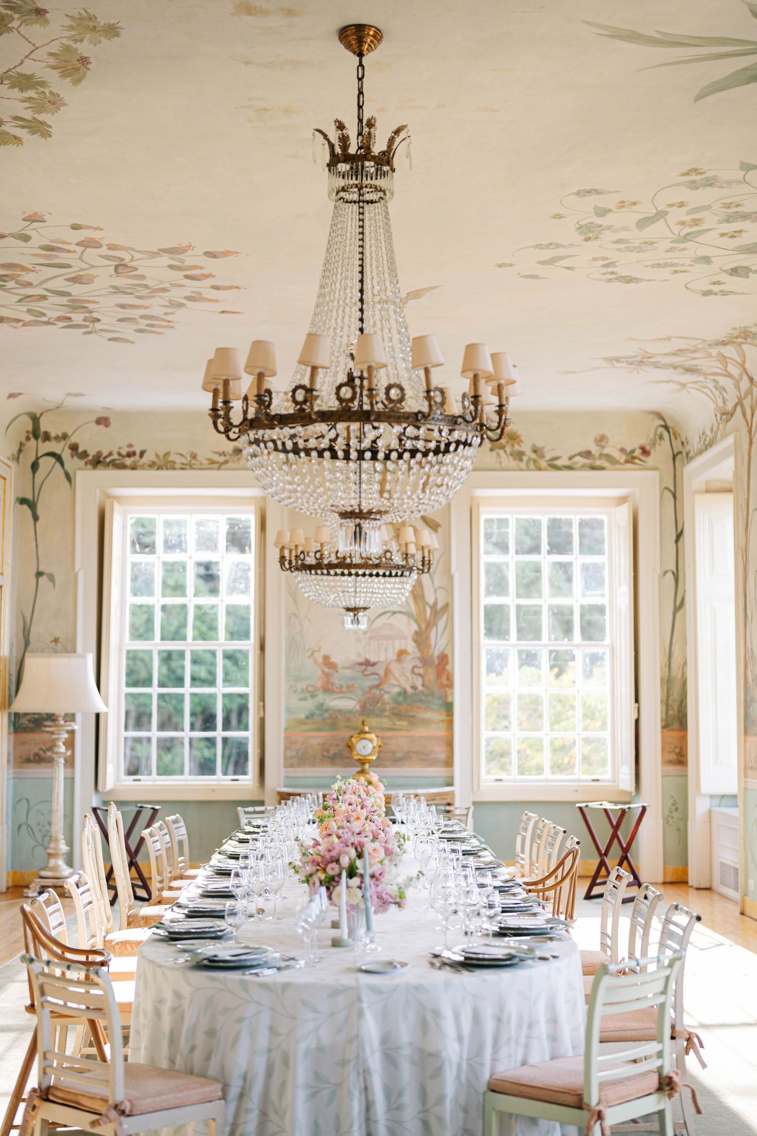 Bright dining space with crystal chandeliers, white table settings, and pastoral wall murals creating an elegant atmosphere.