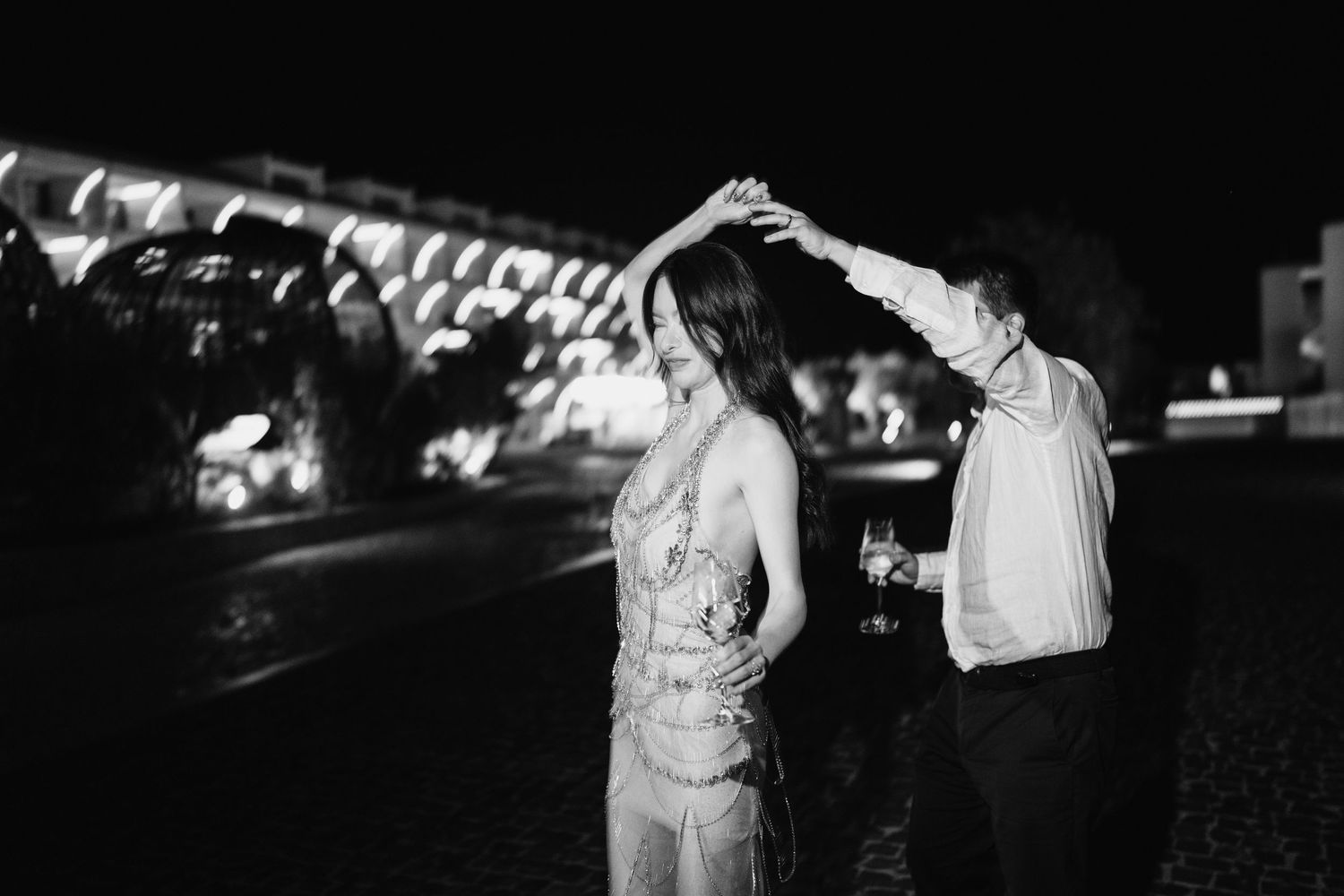 Couple dancing together at night with decorative lights in the background.