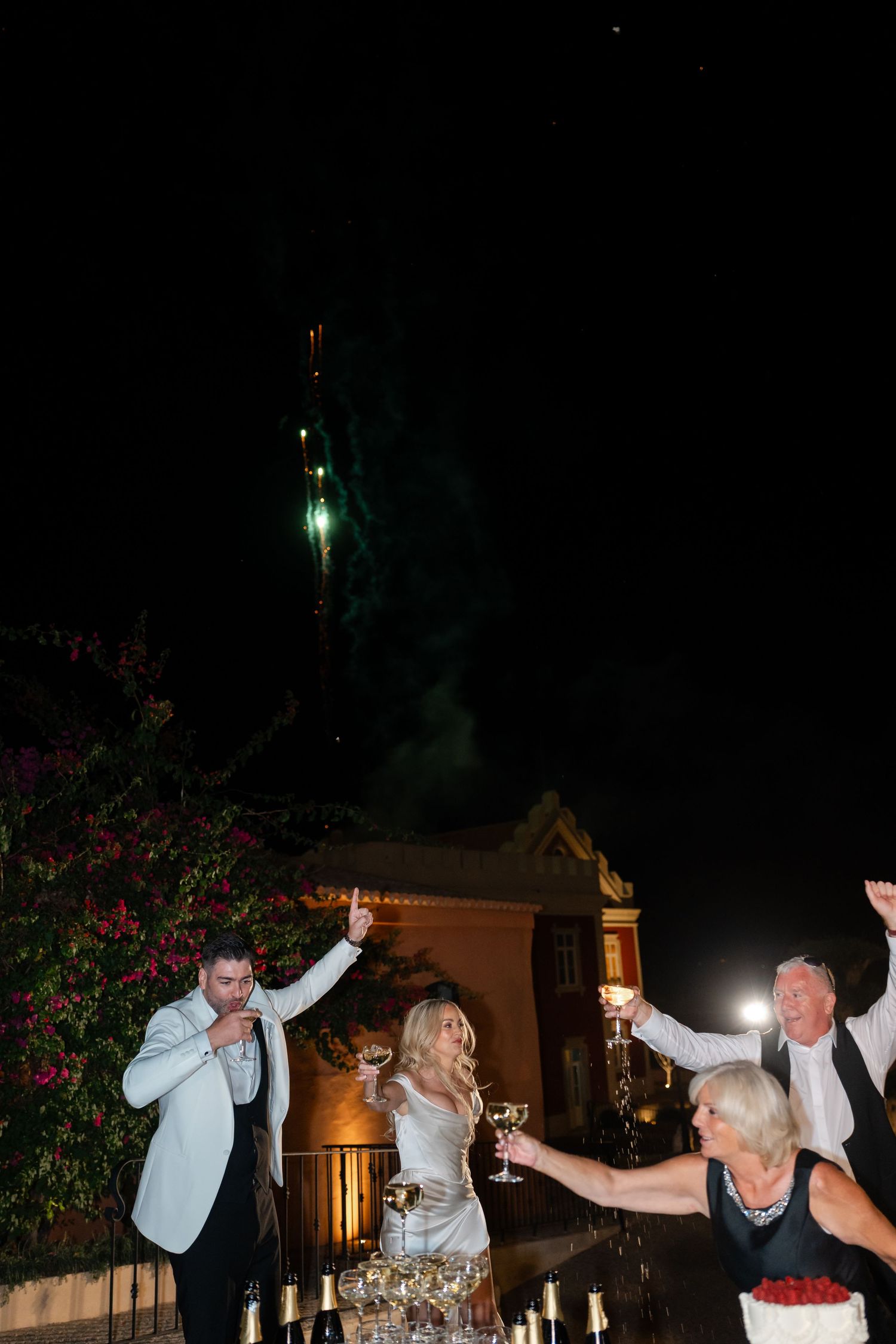 Newlyweds celebrating with champagne tower and cake during nighttime wedding reception.