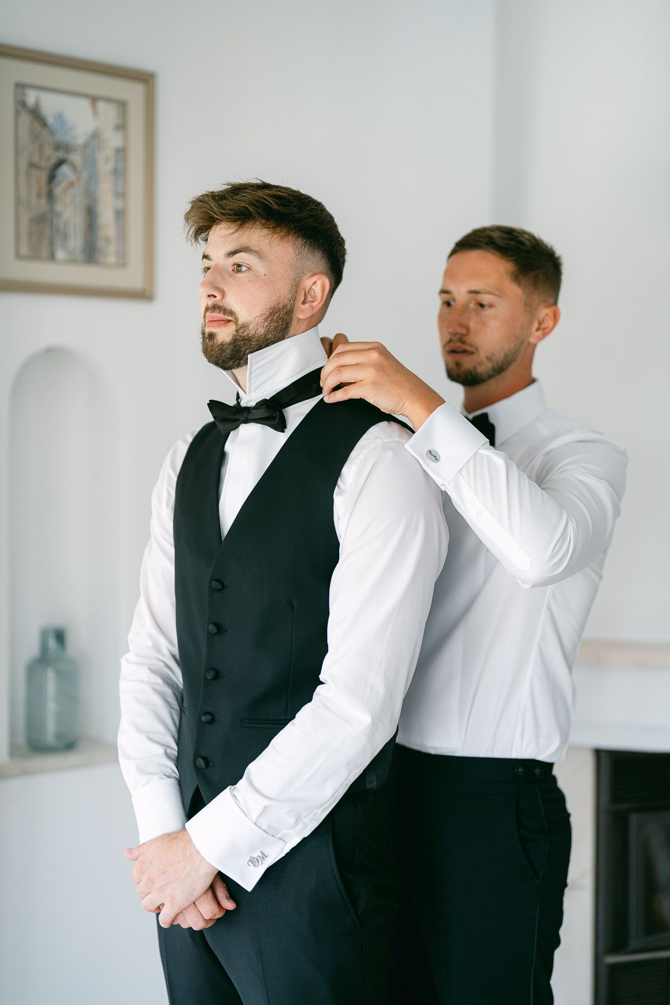 Groomsmen in formal attire getting ready for a wedding, wearing white shirts and black vests.