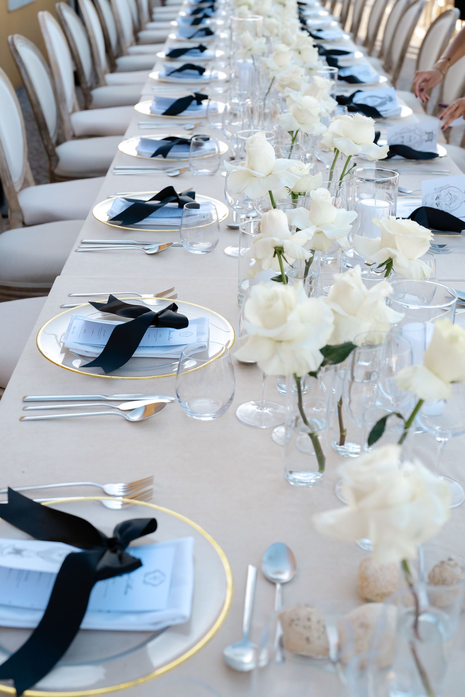 Elegant table setting with white roses, gold-rimmed plates, and black ribbon napkins for a formal event.