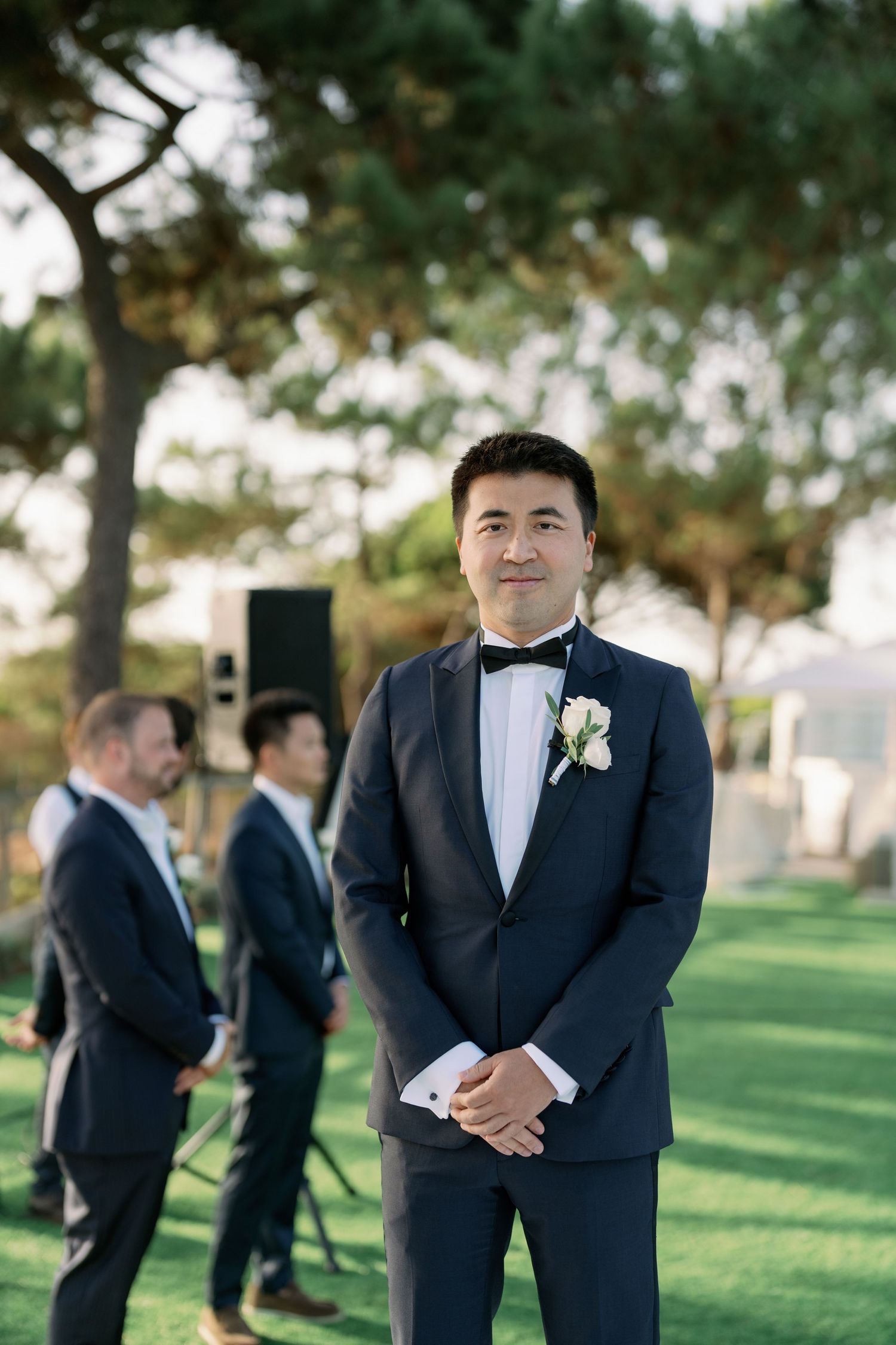 Groomsman in classic navy tuxedo with boutonniere at outdoor garden wedding.