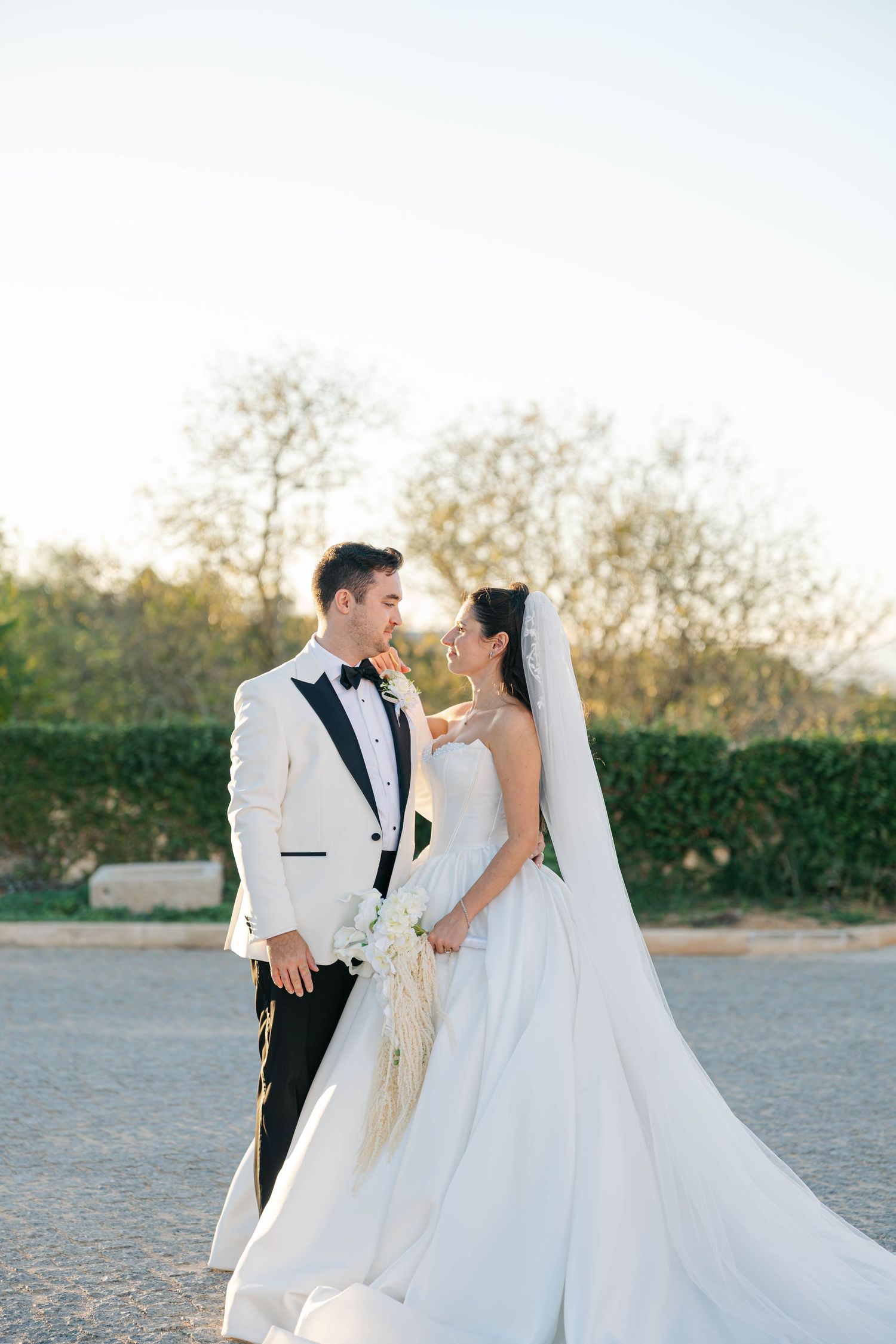 A bride and groom share an intimate moment at sunset in a garden setting with a flowing white wedding gown.
