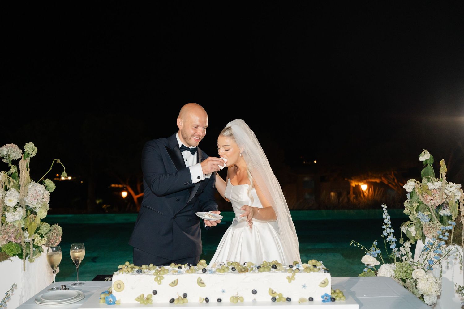 Wedding couple sharing a moment at their reception table with floral centerpieces and evening lighting.