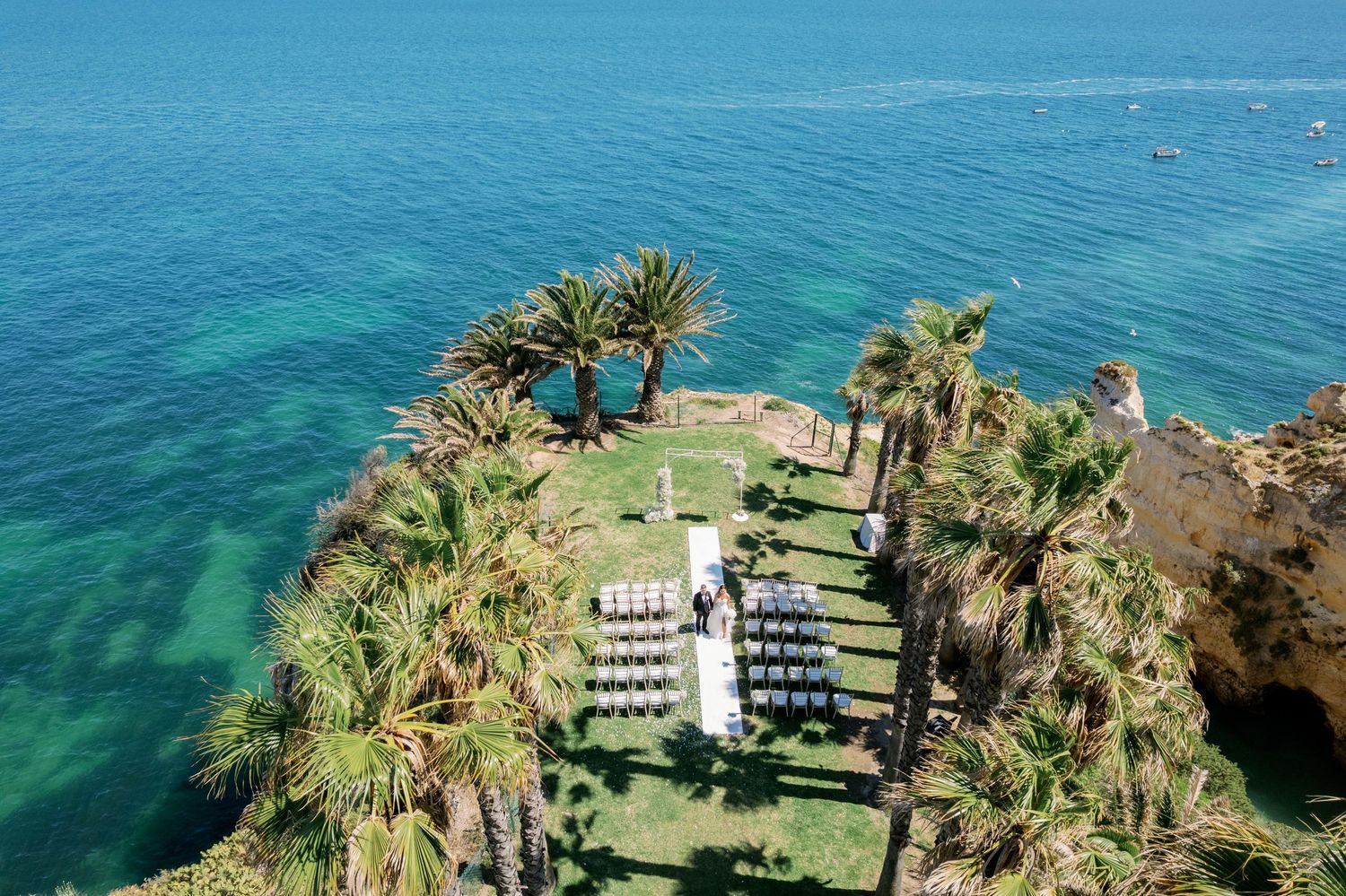 Aerial panoramic view of a coastal resort with palm trees and turquoise Mediterranean waters stretching to the horizon.