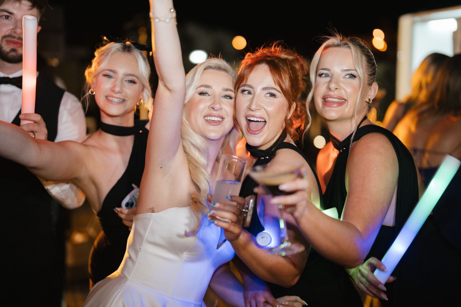 Wedding guests dancing and celebrating with glow sticks at night.