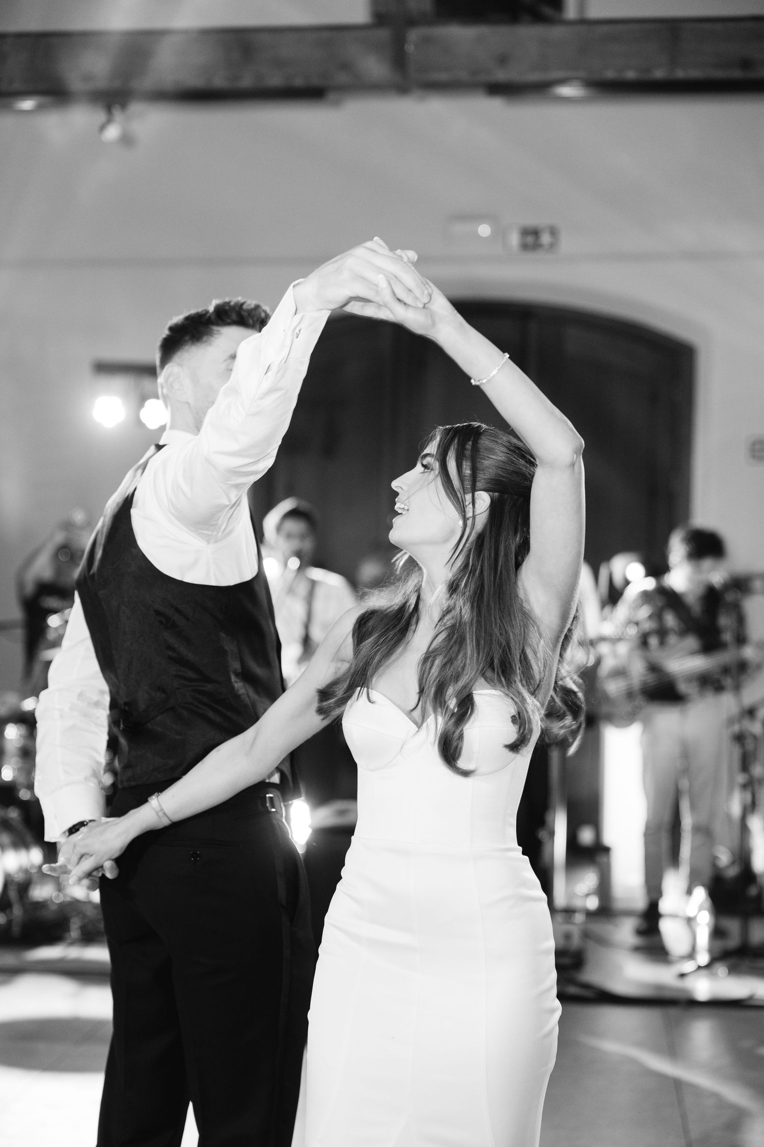 A couple performs an elegant dance move at their wedding reception with raised arms in formal attire.