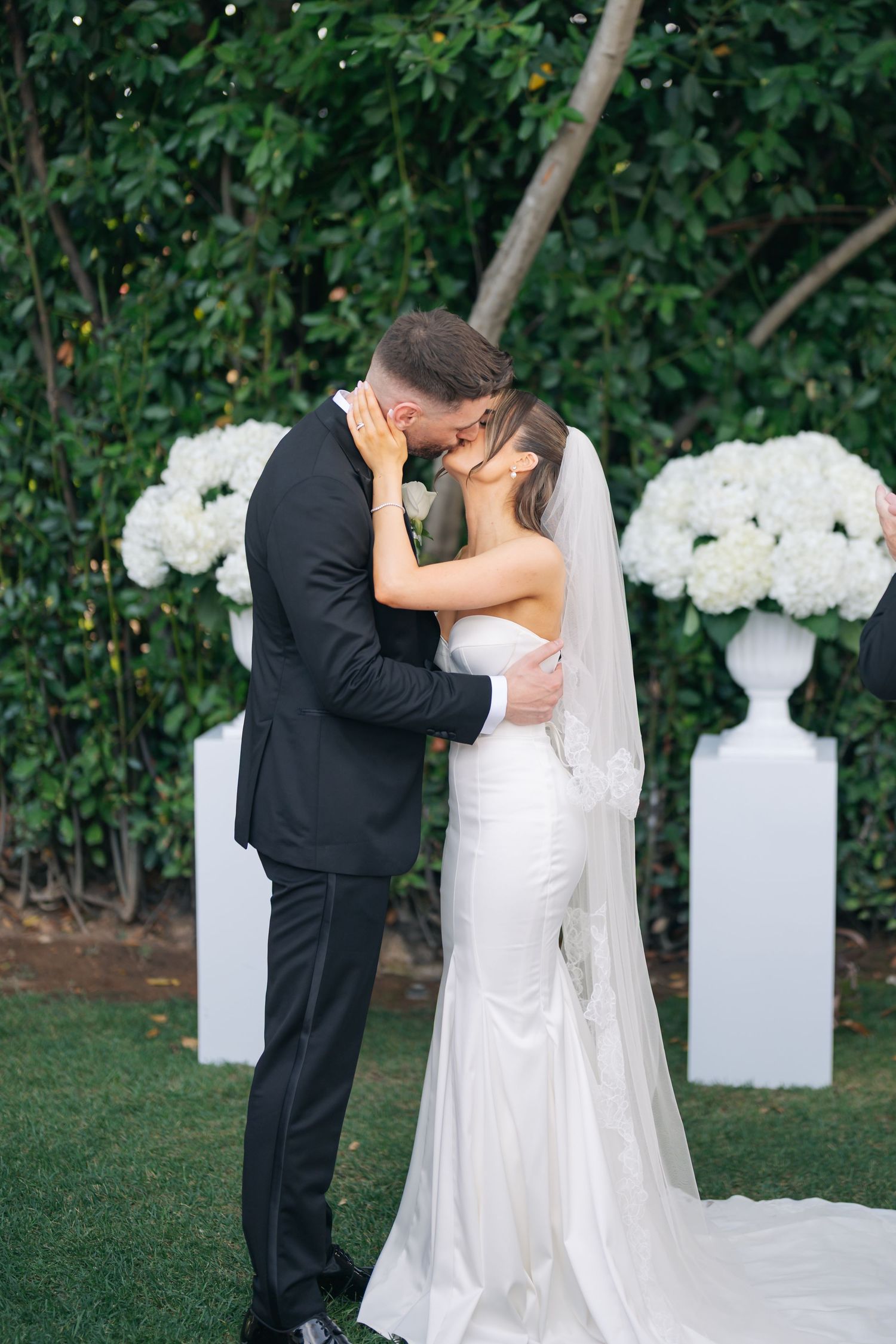 Romantic wedding portraits with white floral urns decorating the outdoor garden setting.