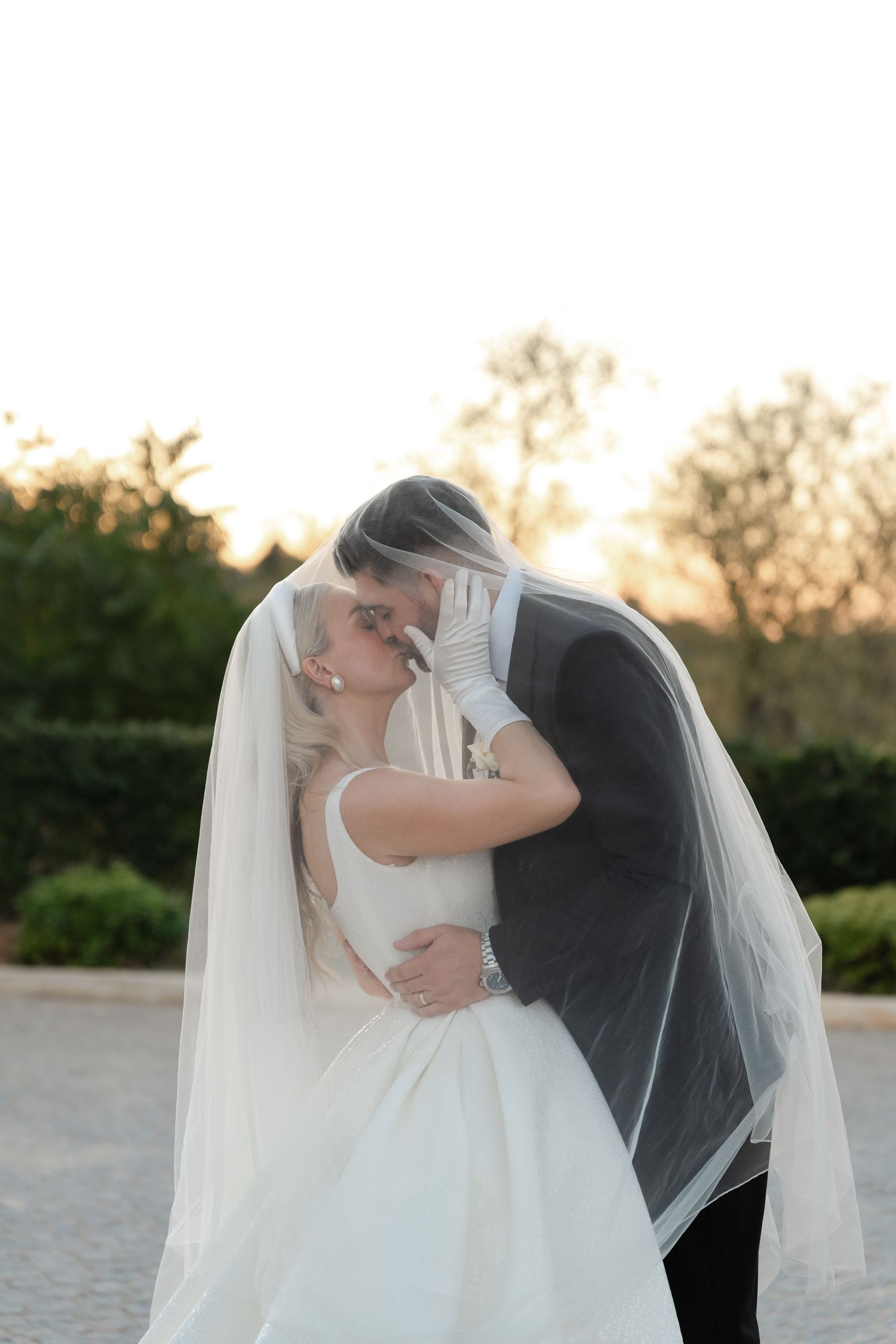 A tender wedding moment captured during golden hour with flowing white veil.