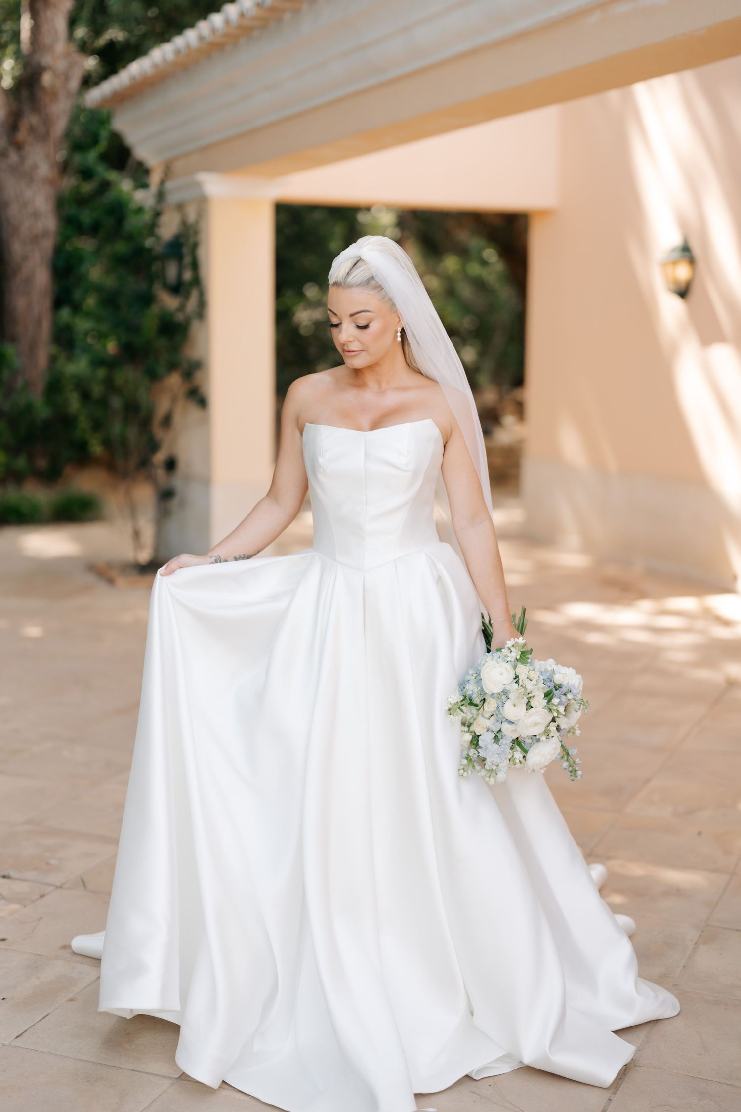 Elegant white wedding dress with full skirt photographed in outdoor Mediterranean setting.